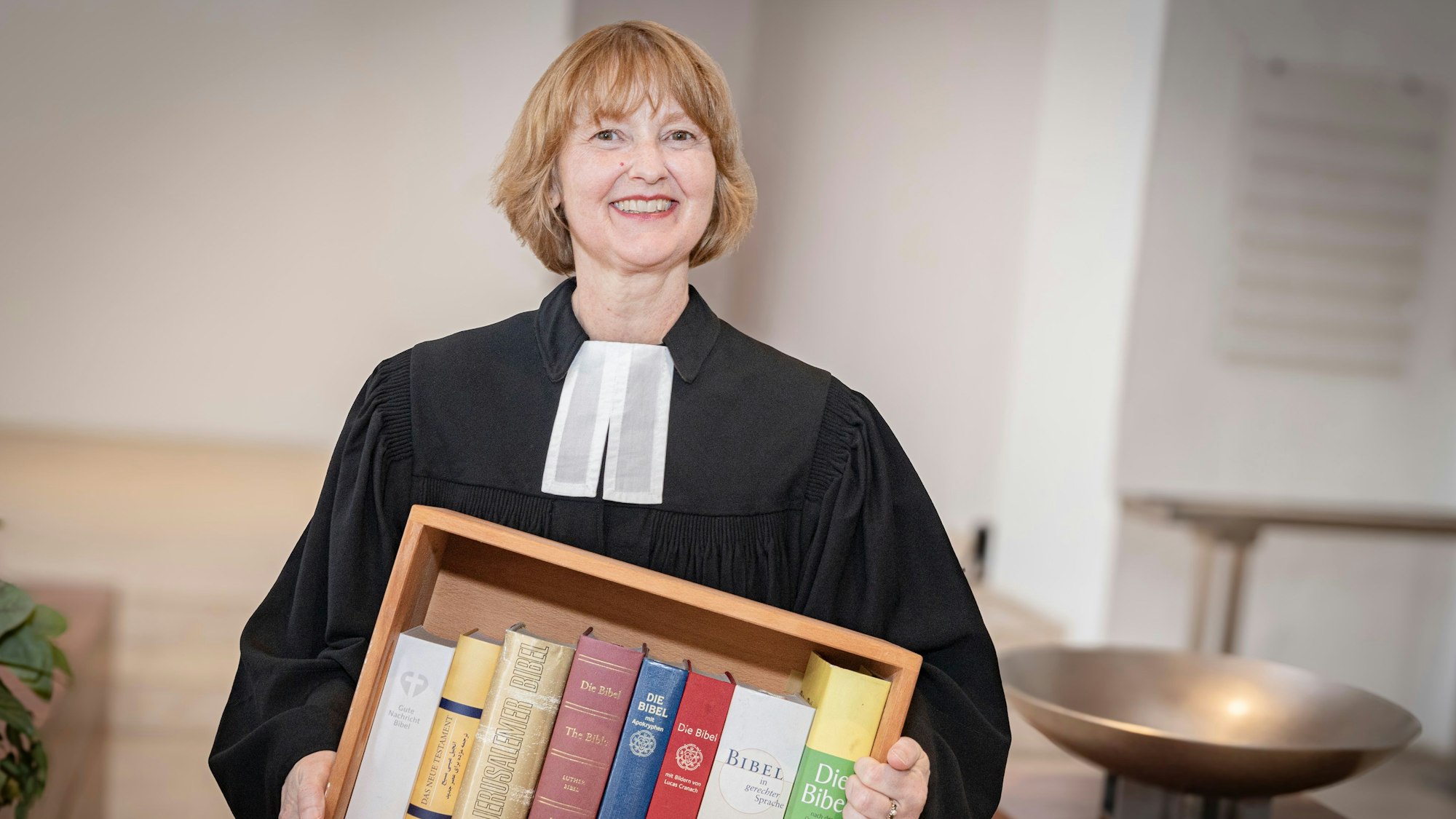 Almut van Niekerk lächelt in die Kamera und hält einen Kasten mit Bibeln in der Hand.
