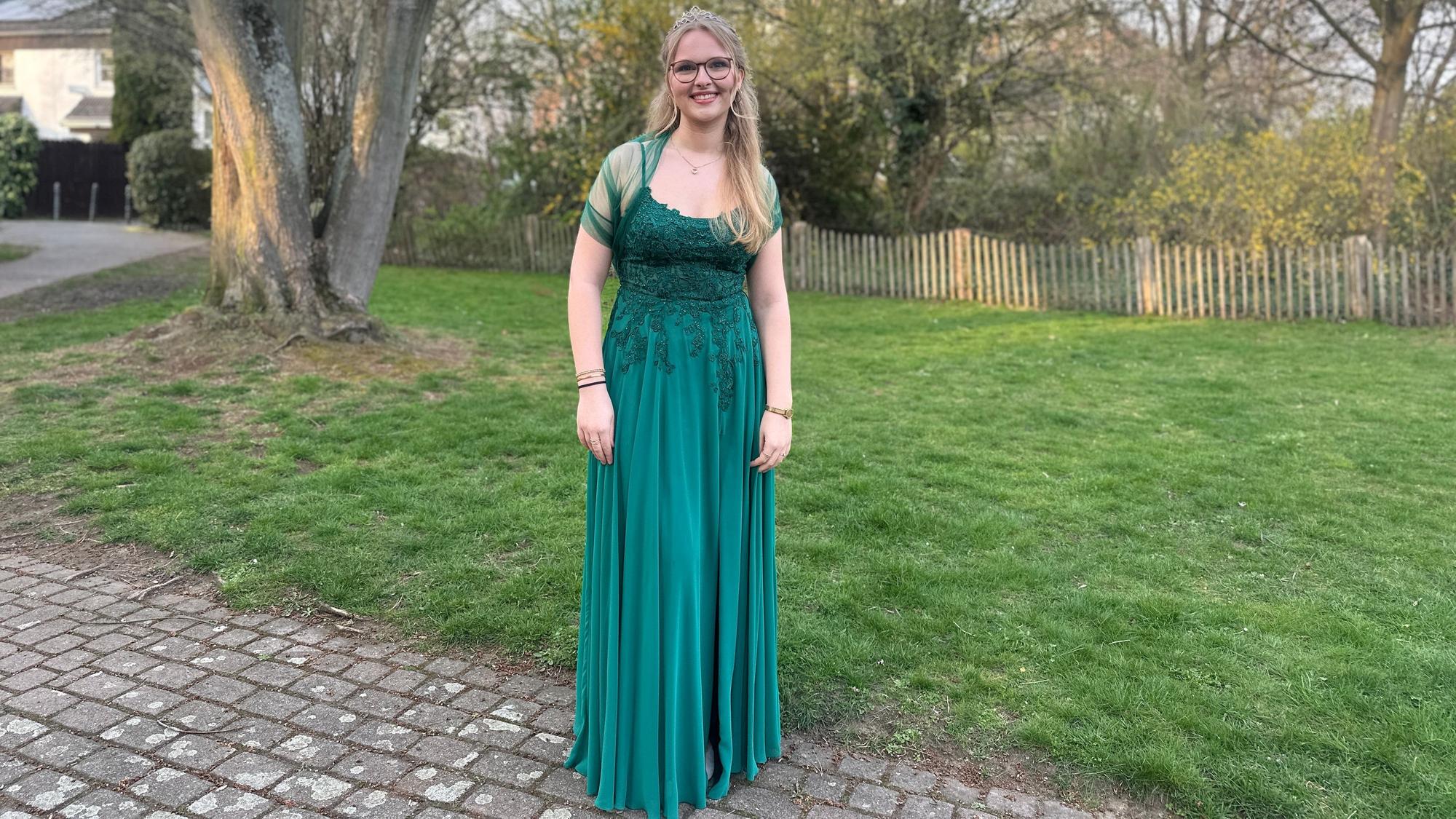 Maikönigin Emma Klaassen trägt ein grünes Ballkleid und steht am Rand einer Wiese.