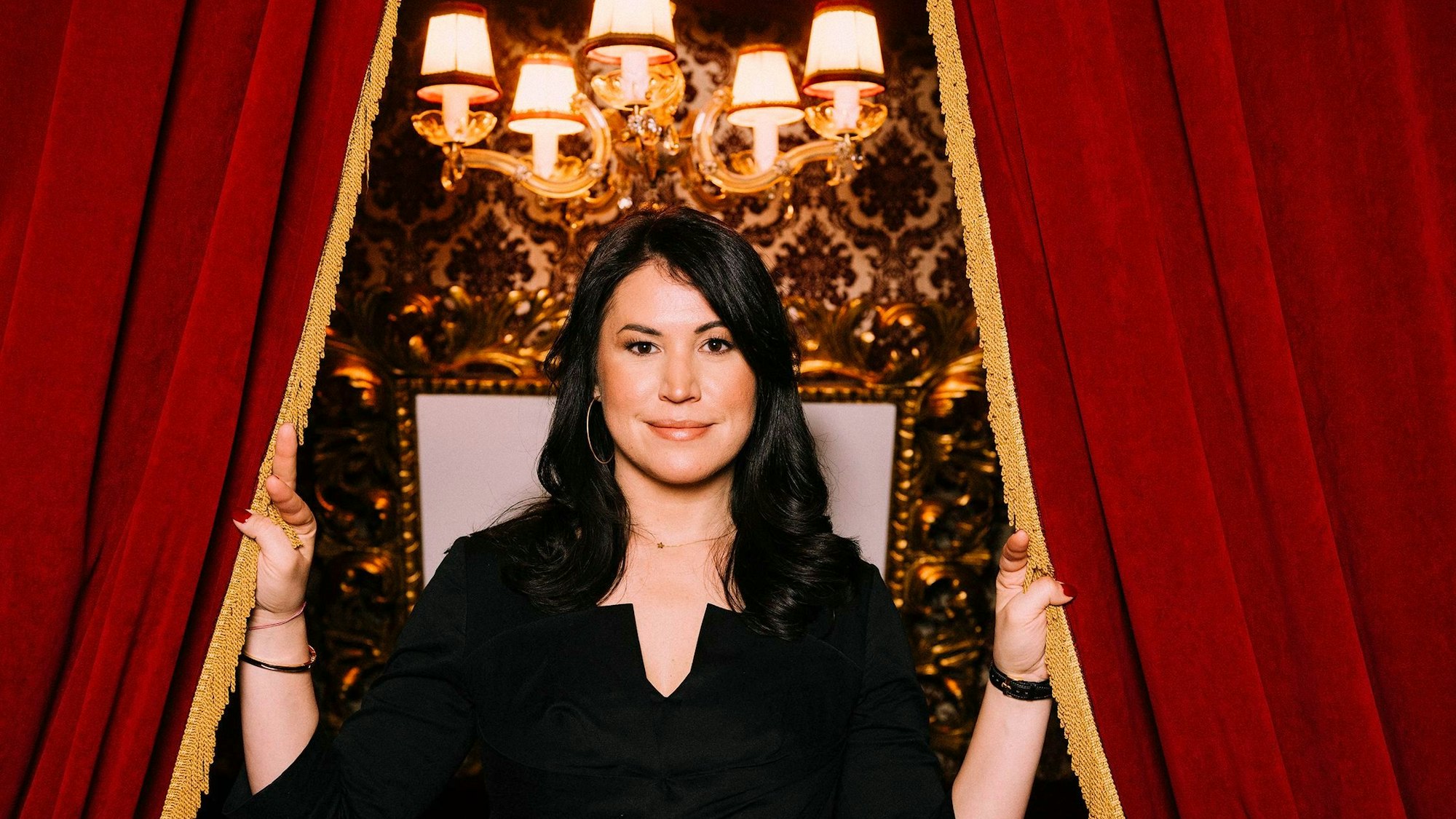 Die Autorin Vea Kaiser hält die Bahnen eines roten Vorhangs auseinander.