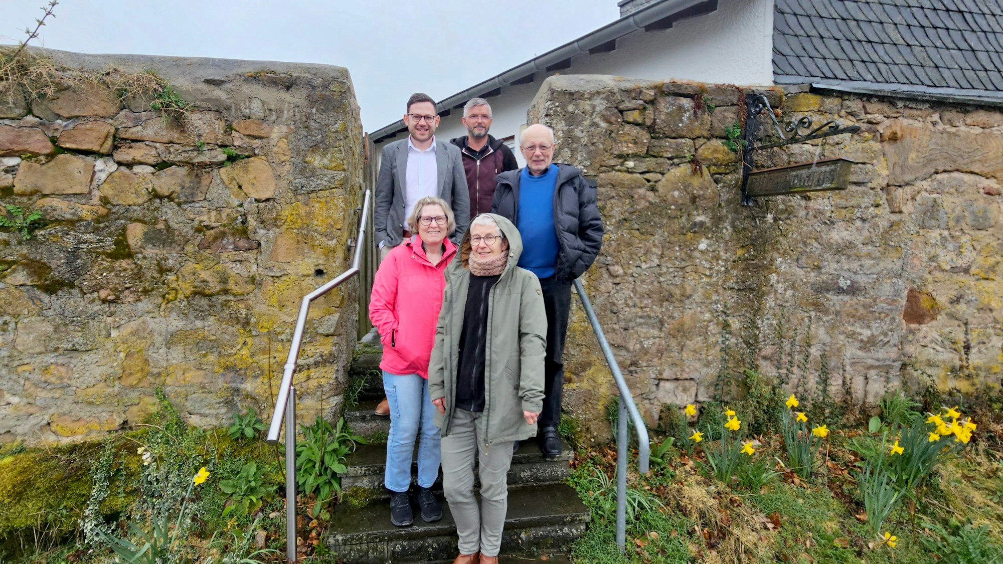 Zwei Frauen und dahinter drei Männer stehen auf einer Treppe am Eingang zum Bürgerhaus. Links und rechts ist eine alter Mauer zu sehen.