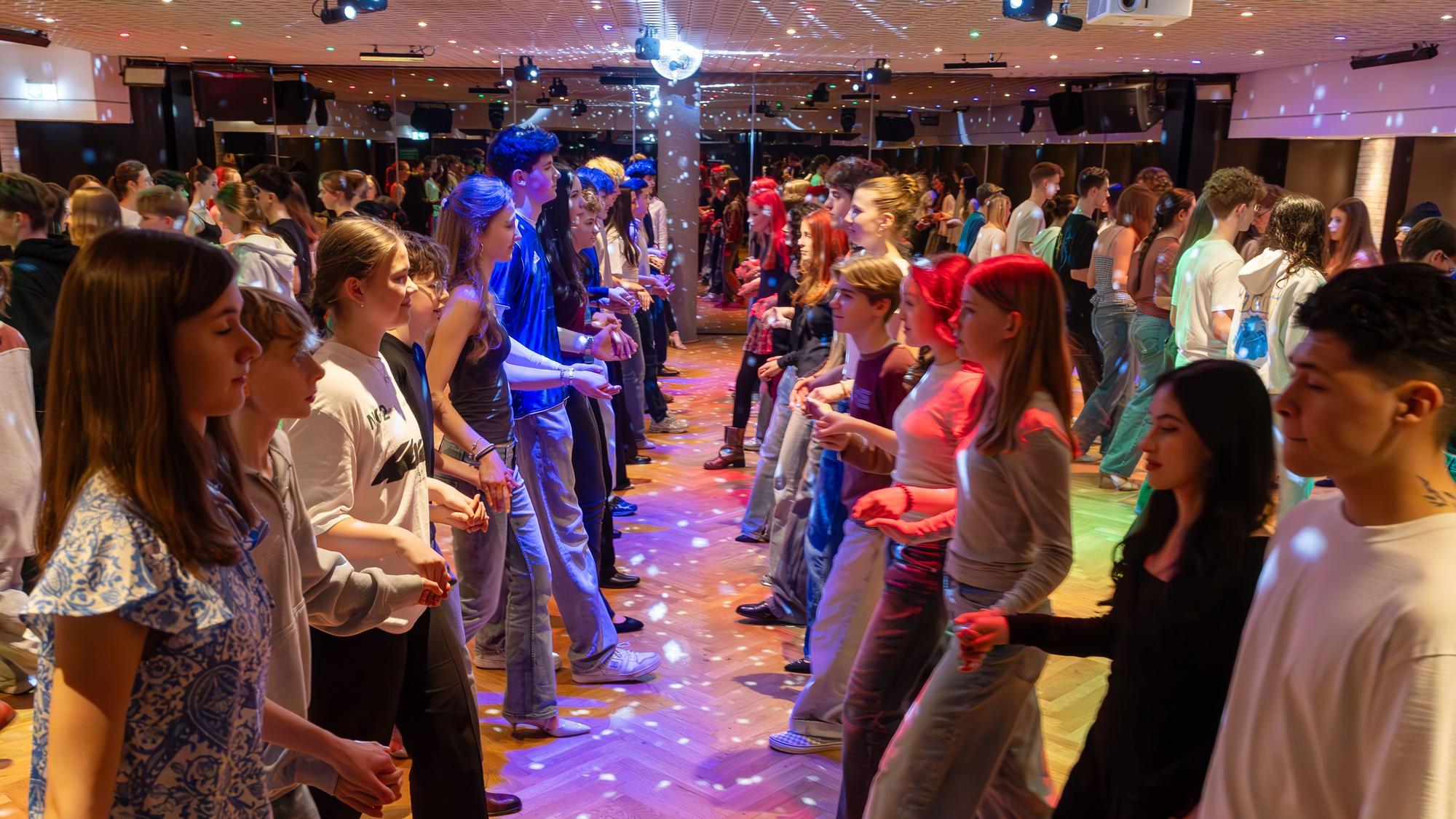 Die Fledermausquadrille wird in der Tanzschule van Hasselt geprobt, in der Mitte der linken Seite tanzen Emilia und Joscha. In dem Saal mit der Discobeleuchtung werden auch Partys gefeiert.