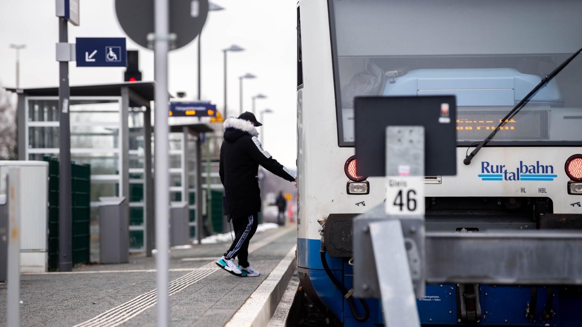 Ein Mann in Freizeitkleidung und Winterjacke steight am Bahnhof in Zülpich in einen Zug ein, auf dem Rurtalbahn steht.