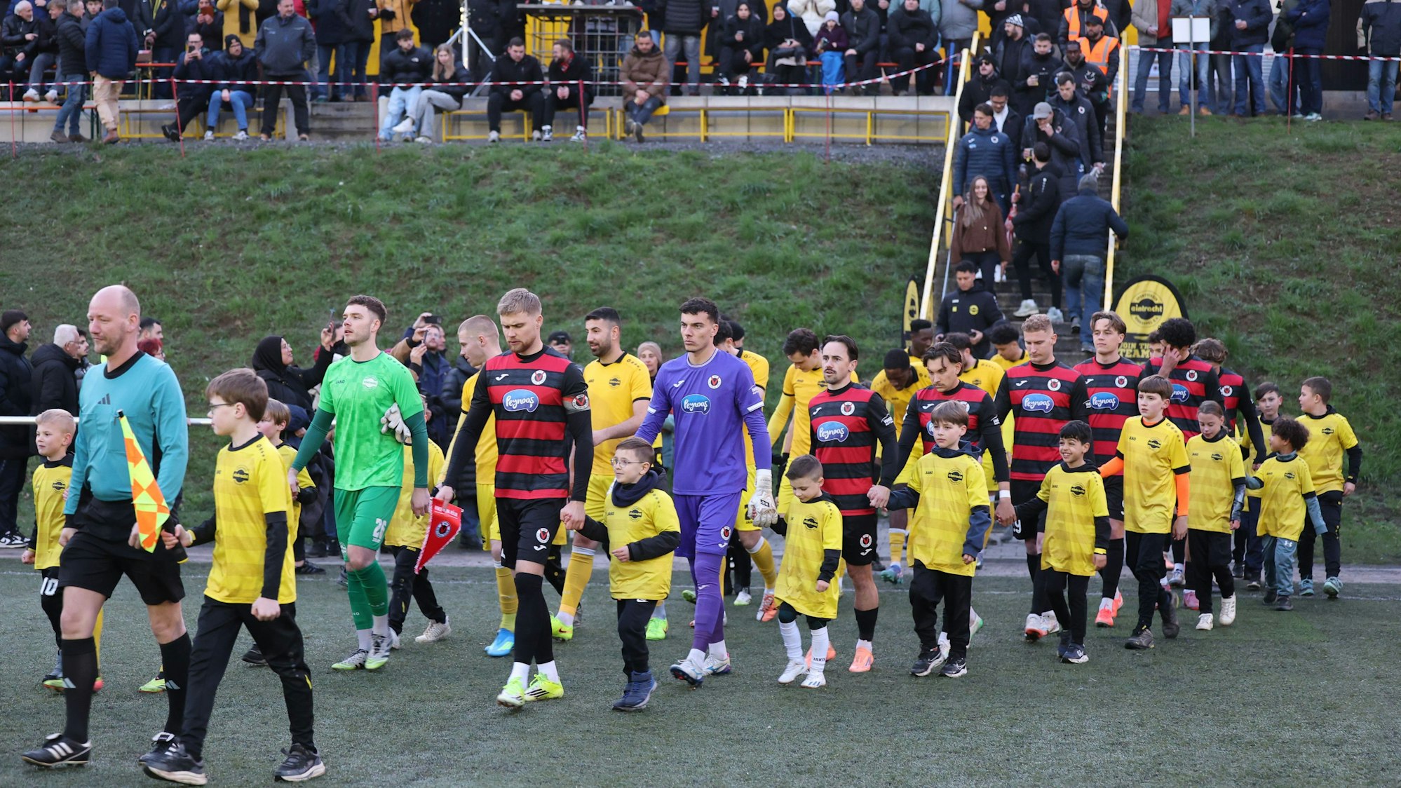 Die beiden Mannschaften laufen mit den Nachwuchskicker ins Achim-Lammers-Stadion in Köttingen ein.