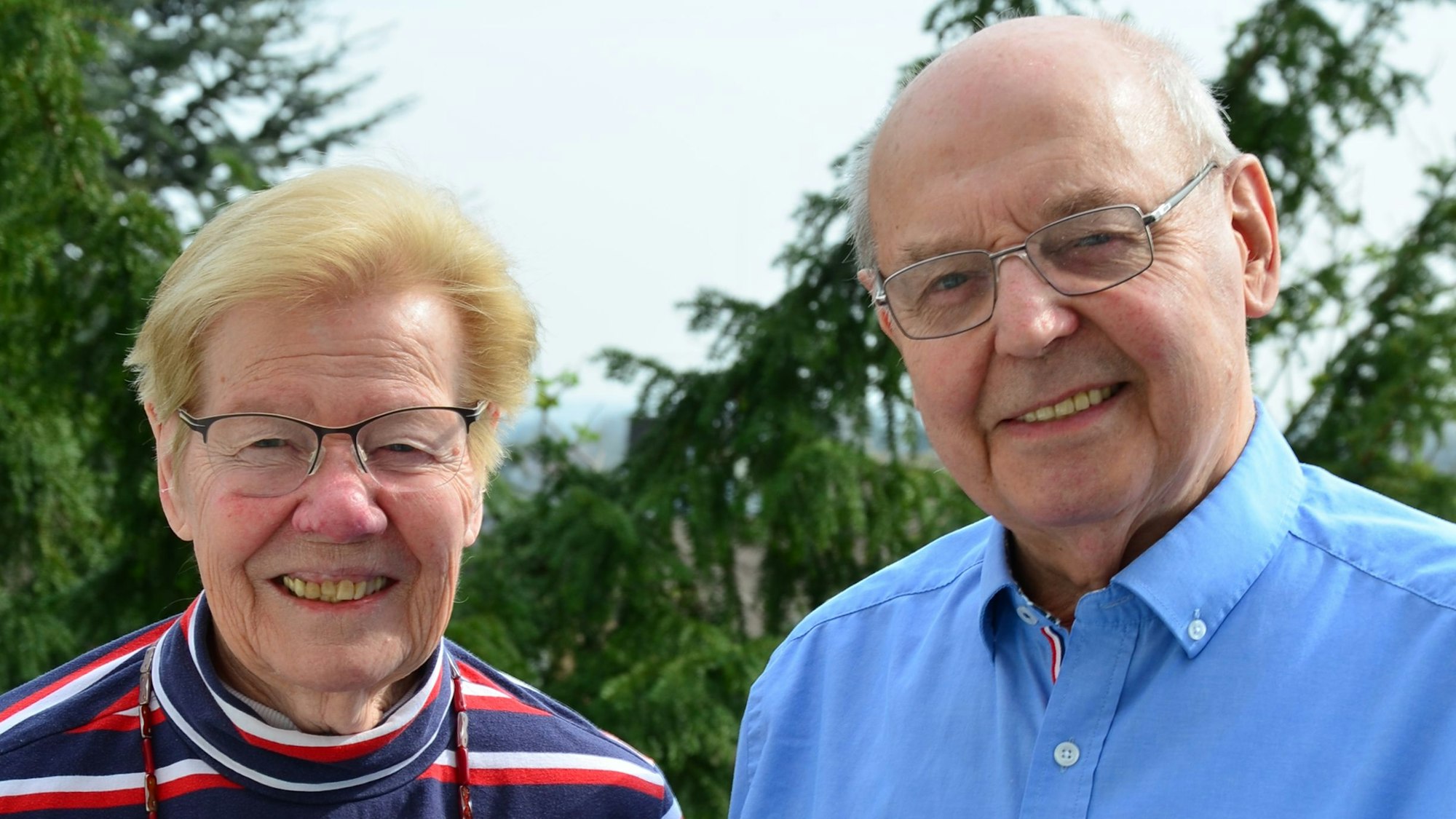 Ein Mann und eine Frau stehen vor Bäumen und lächeln.