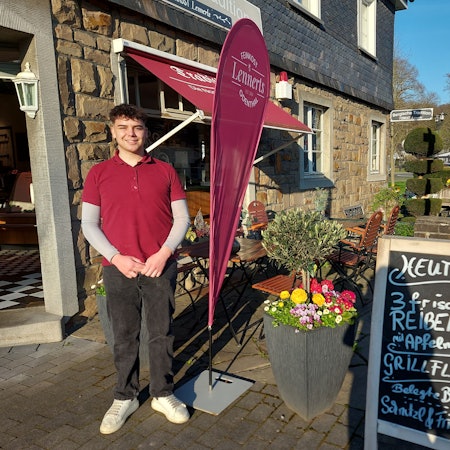 Ein junger Mann steht vor einer kleinen Landmetzgerei.