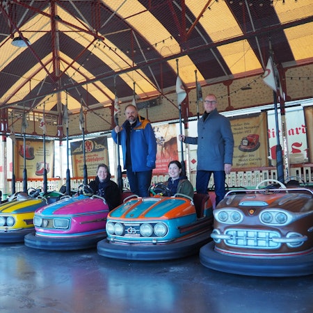 Die bunten kleinen Autos stehen in einer Reihe, Daniel Manner und Carsten Vorwig stehen hinten und halten sich an der Stange des Stromabnehmers fest, Anne Carl und Margarethe Becker sitzen in zwei Scootern.