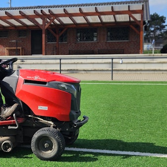 Ein Mann sitzt auf einem Minitraktor auf einem Sportplatz.
