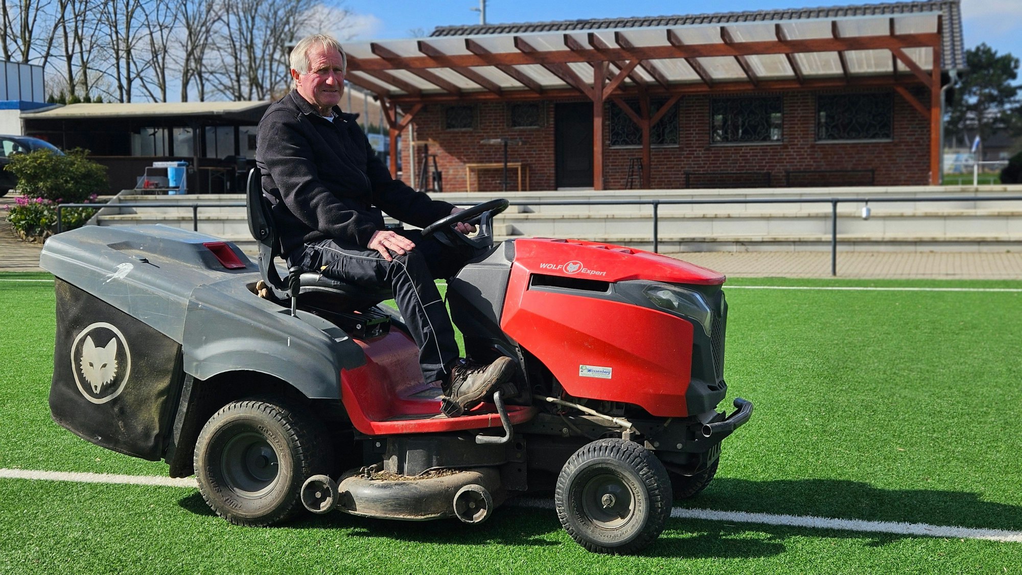 Ein Mann sitzt auf einem Minitraktor auf einem Sportplatz.
