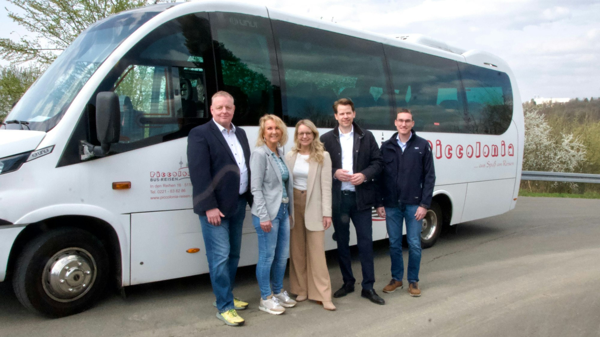 Fünf Personen stehen vor einem Bus und lächeln.