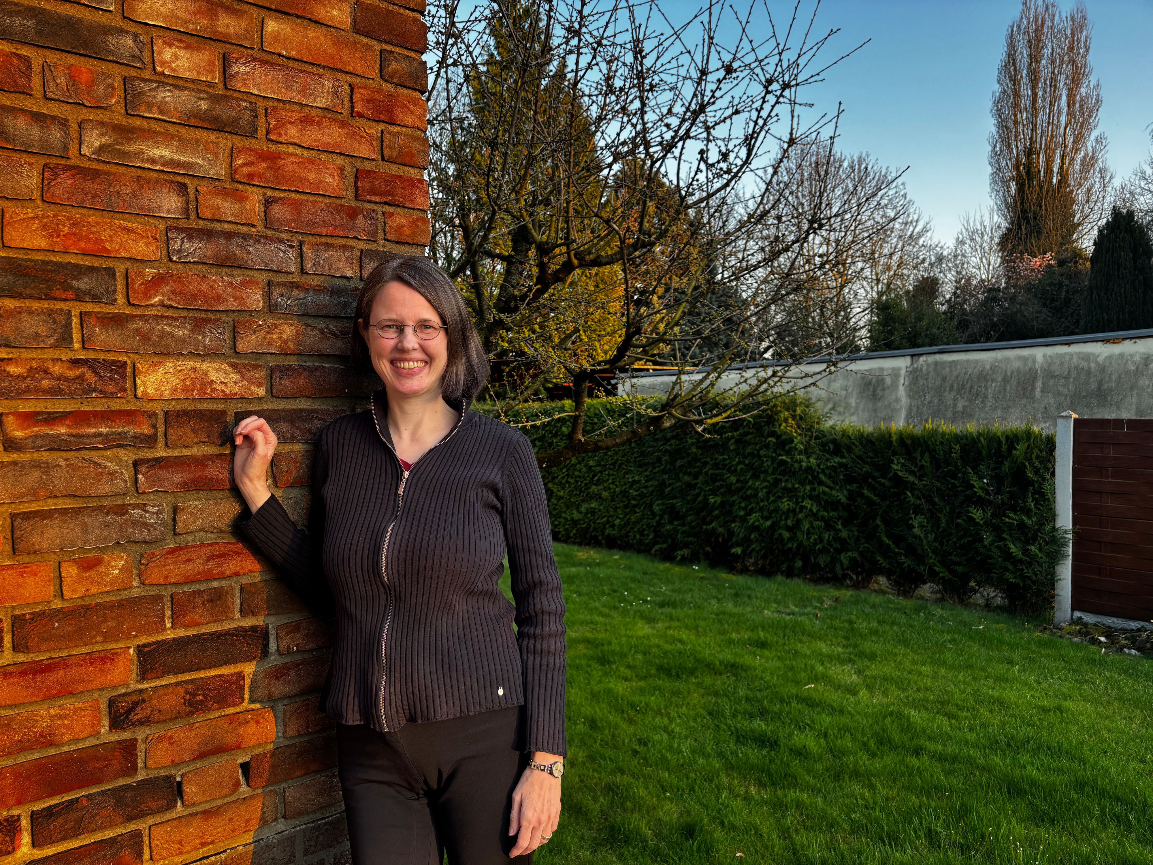 Carolin Ehrlichmann steht in ihrem Garten und lehnt sich an die Hauswand.