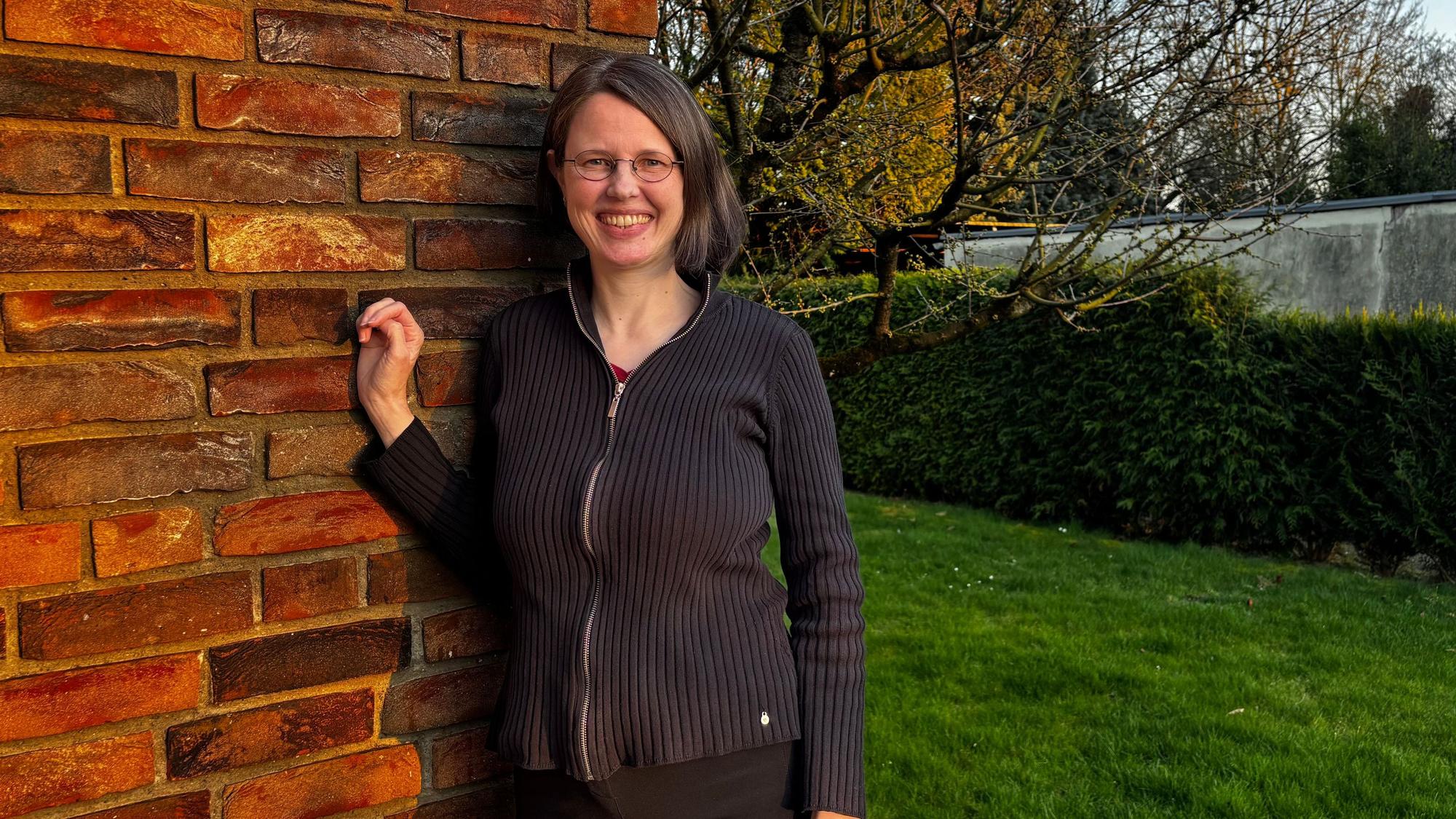 Carolin Ehrlichmann steht in ihrem Garten und lehnt sich an die Hauswand.