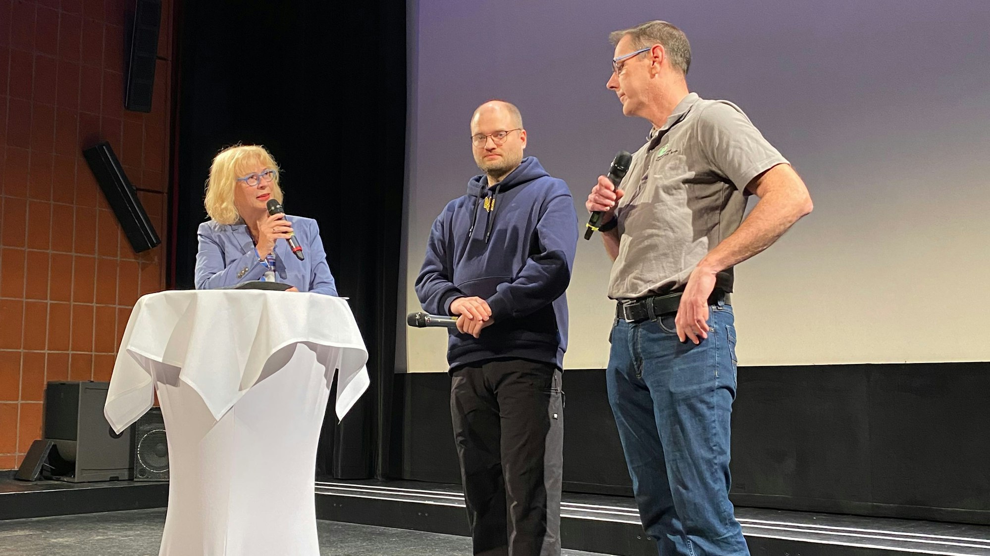 Moderatorin Doro Dietsch, Regisseur Michael Stadnik und Feuerwehrchef Jörg Köhler stehen vor der Leinwand und sprechen über den Film.