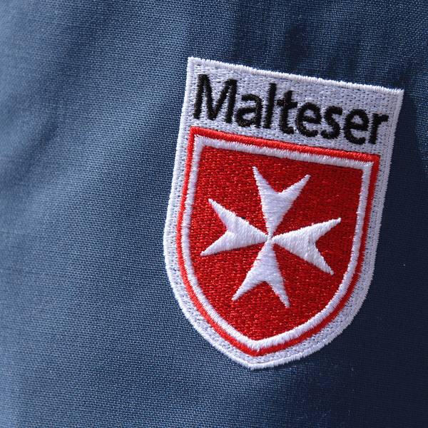 Das Logo der Malteser ist an der Jacke eines Helfers zu sehen.