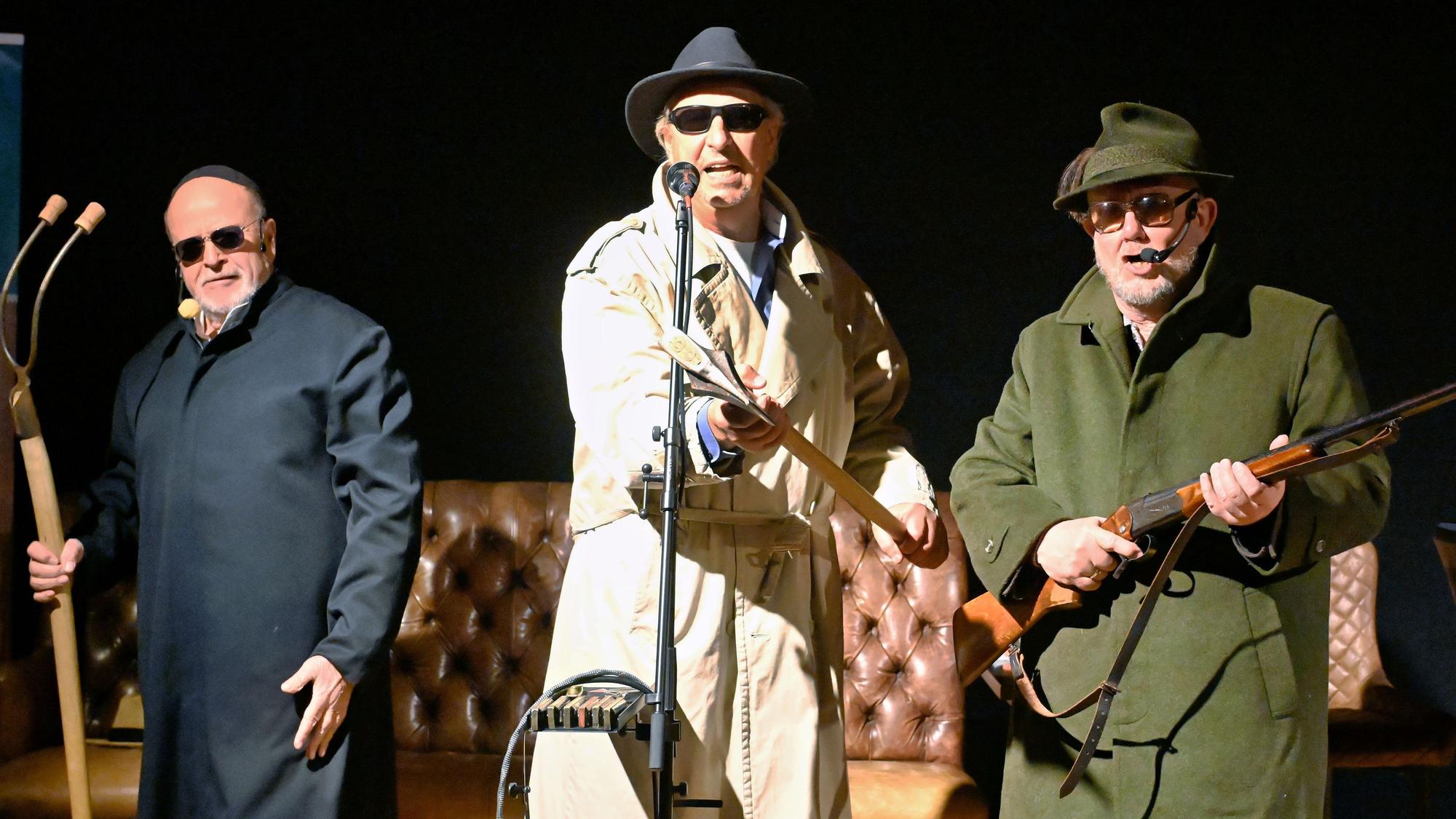 Drei Männer mit Mistgabel, Axt und Gewehr bewaffnet und mit Sonnenbrillen stehen nebeneinander auf der Bühne.