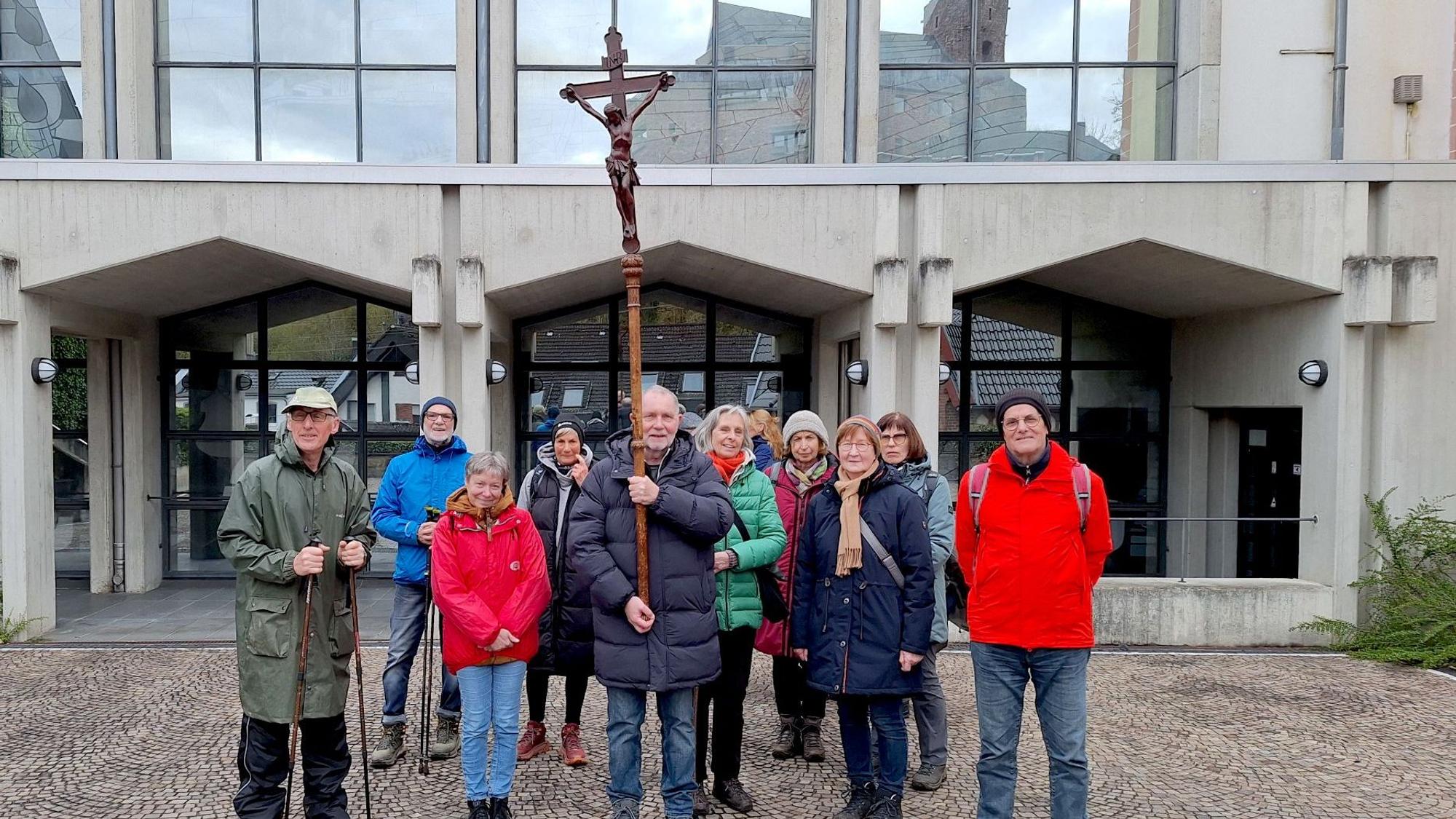 Die Pilgergruppe steht vor der Kirche. Ein Mann hält einen Stab mit einem Kreuz.