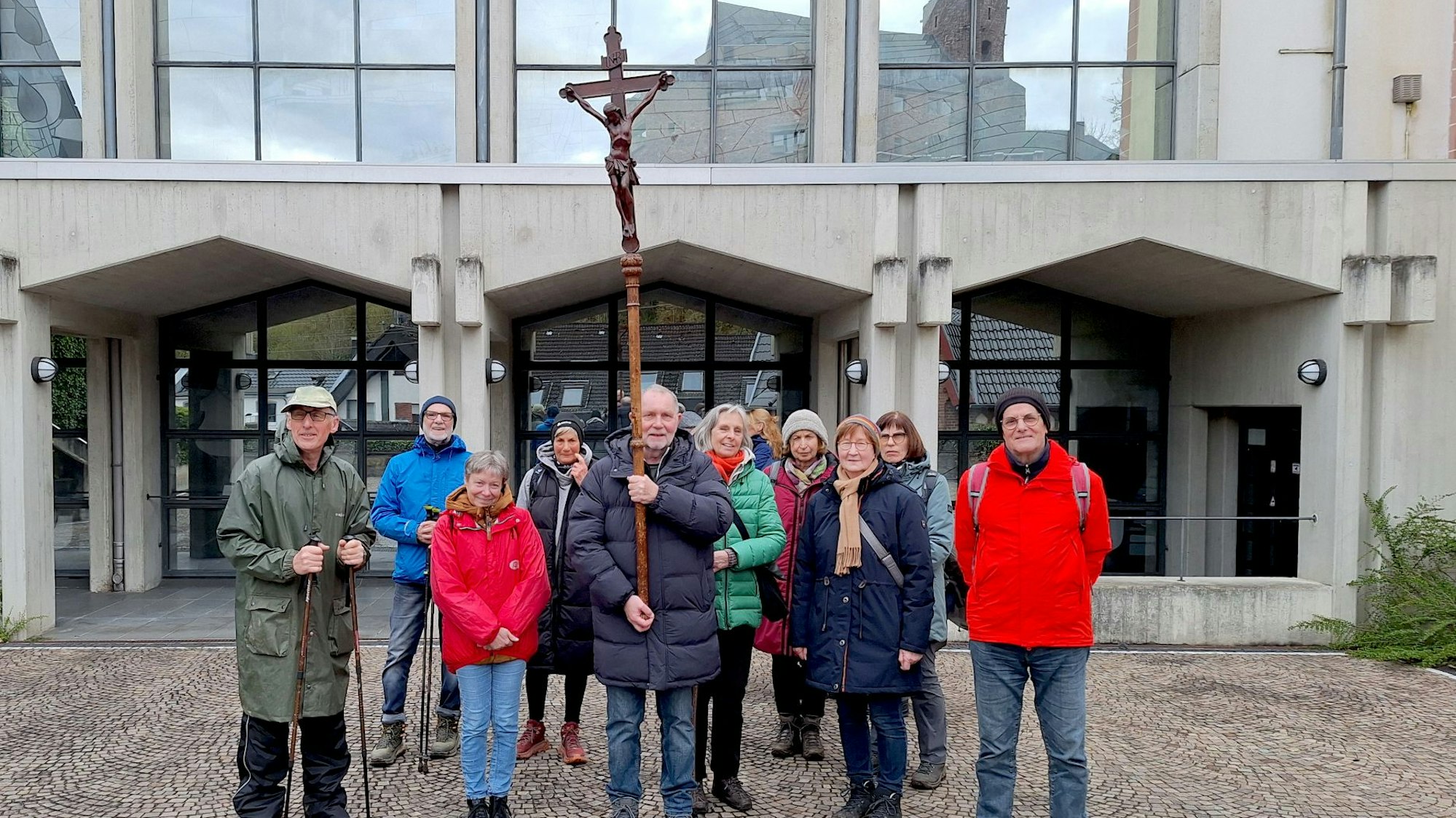 Die Pilgergruppe steht vor der Kirche. Ein Mann hält einen Stab mit einem Kreuz.