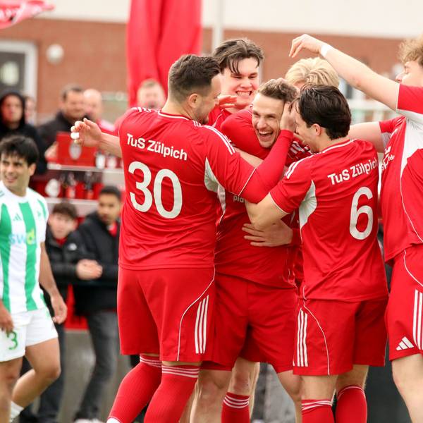 Freudestrahlend steckt Thoma Leßenich inmitten seiner Spieler, die ihm zum Freistoßtor gratulieren.
