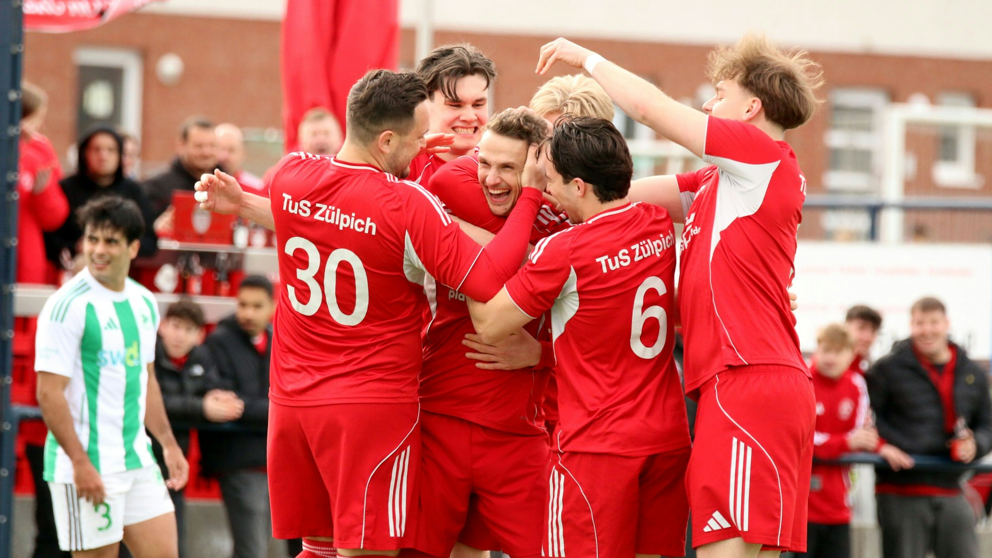 Freudestrahlend steckt Thoma Leßenich inmitten seiner Spieler, die ihm zum Freistoßtor gratulieren.