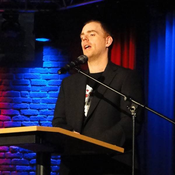 Ein Mann steht an einem Pult und spricht in ein Mikrofon.