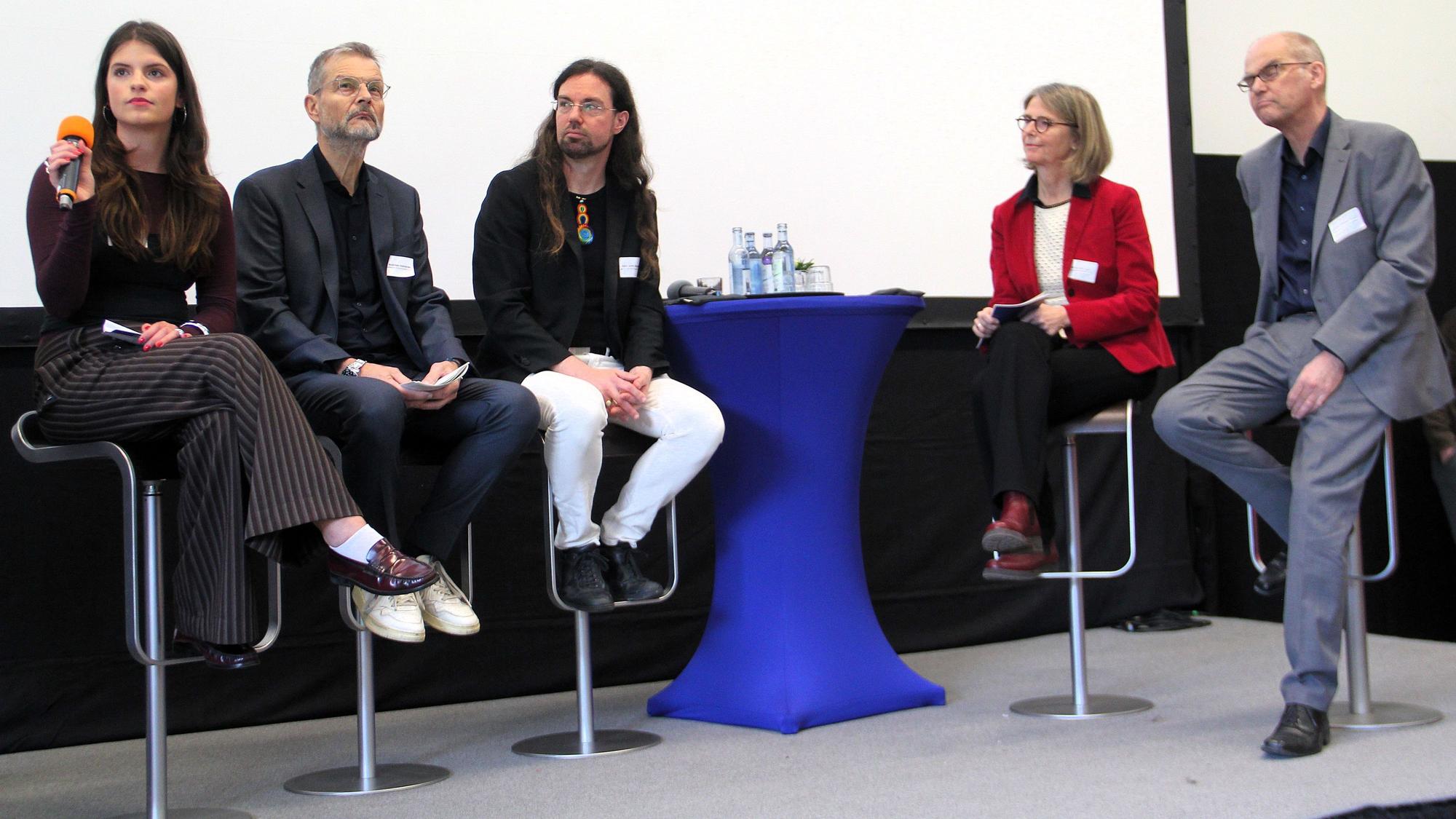 Fünf Menschen sitzen bei einem Podium auf einer Bühne.