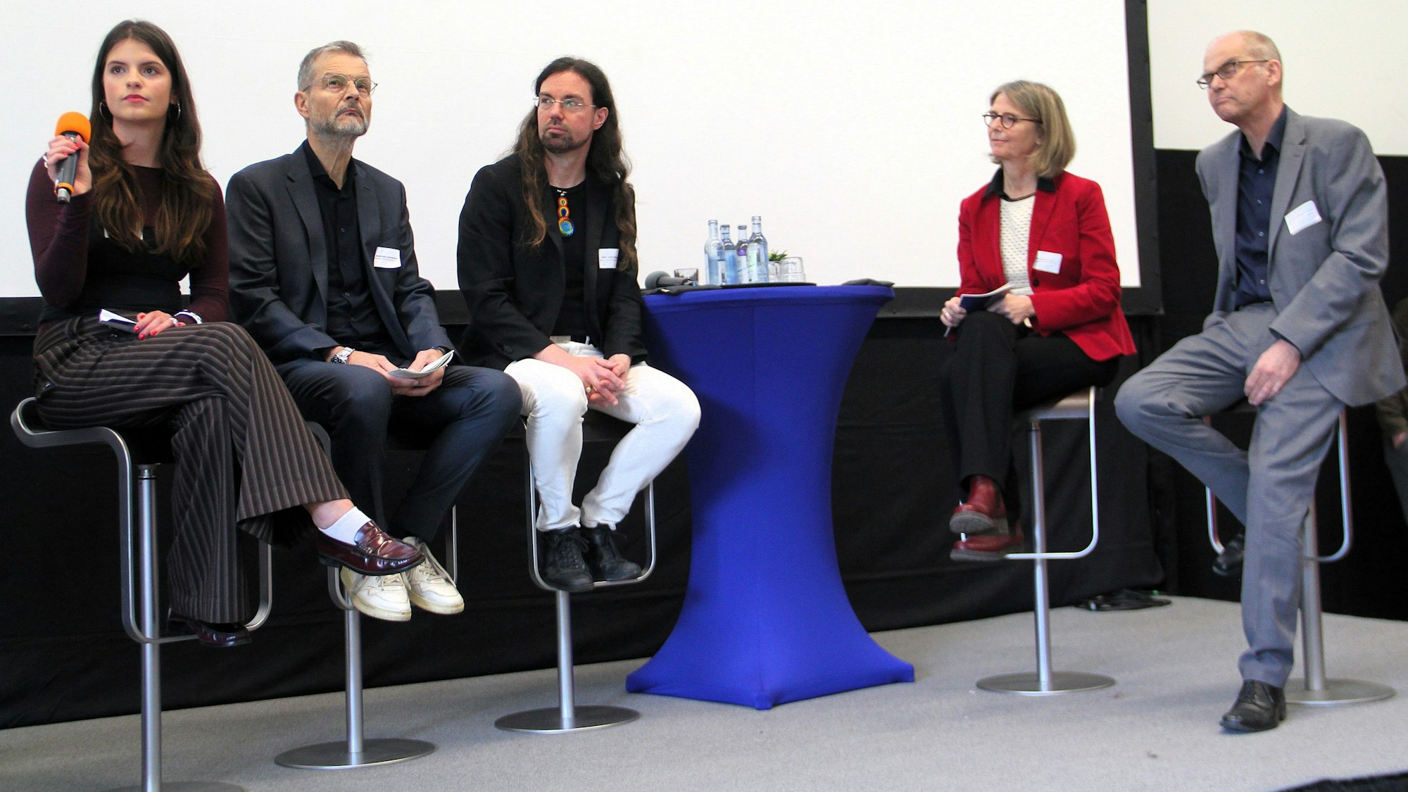 Fünf Menschen sitzen bei einem Podium auf einer Bühne.