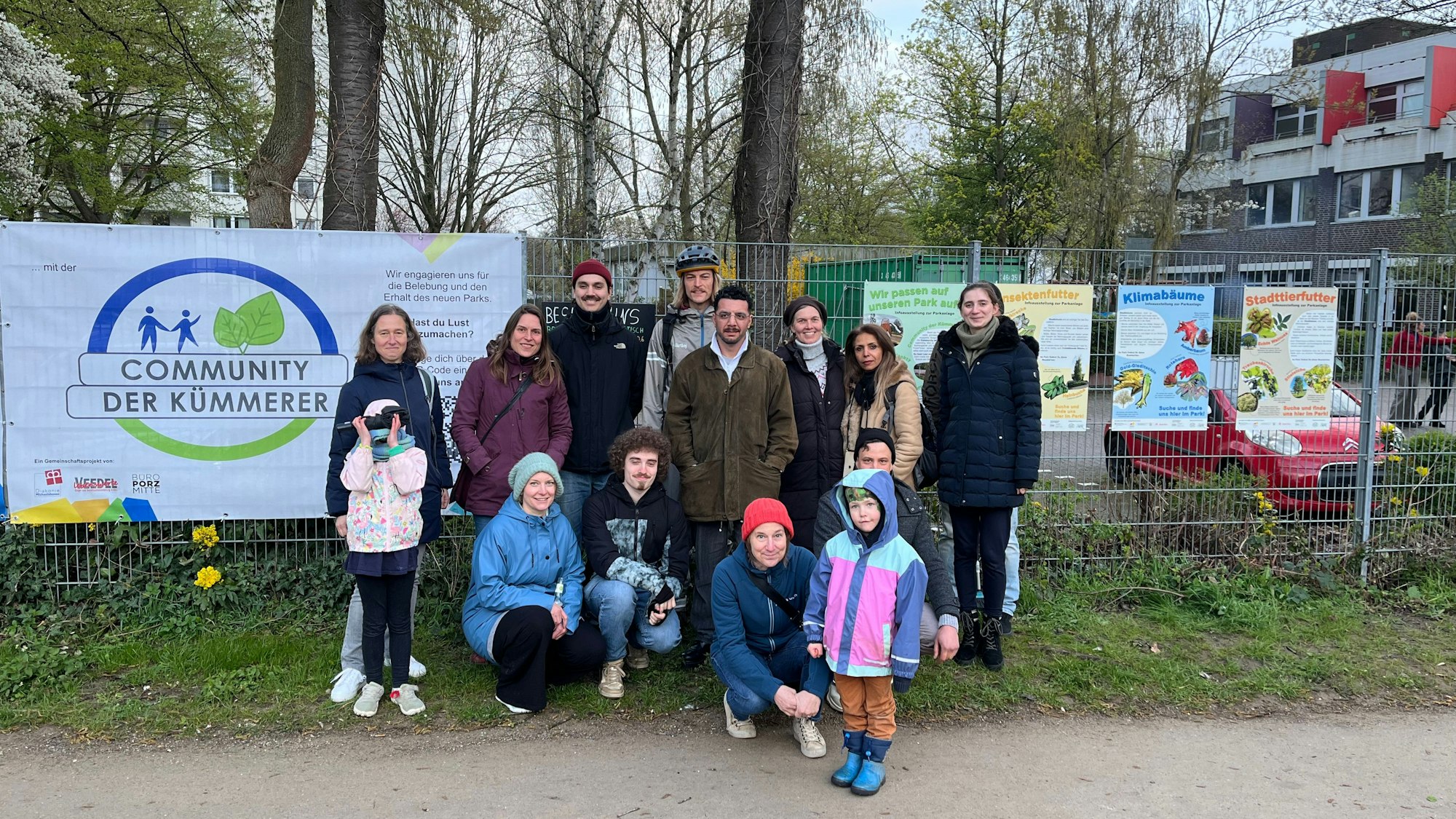Eine Gruppe von Menschen steht vor einem Zaun. Im Hintergrund hängt ein Banner am Zaun mit der Überschrift Community der Kümmerer.