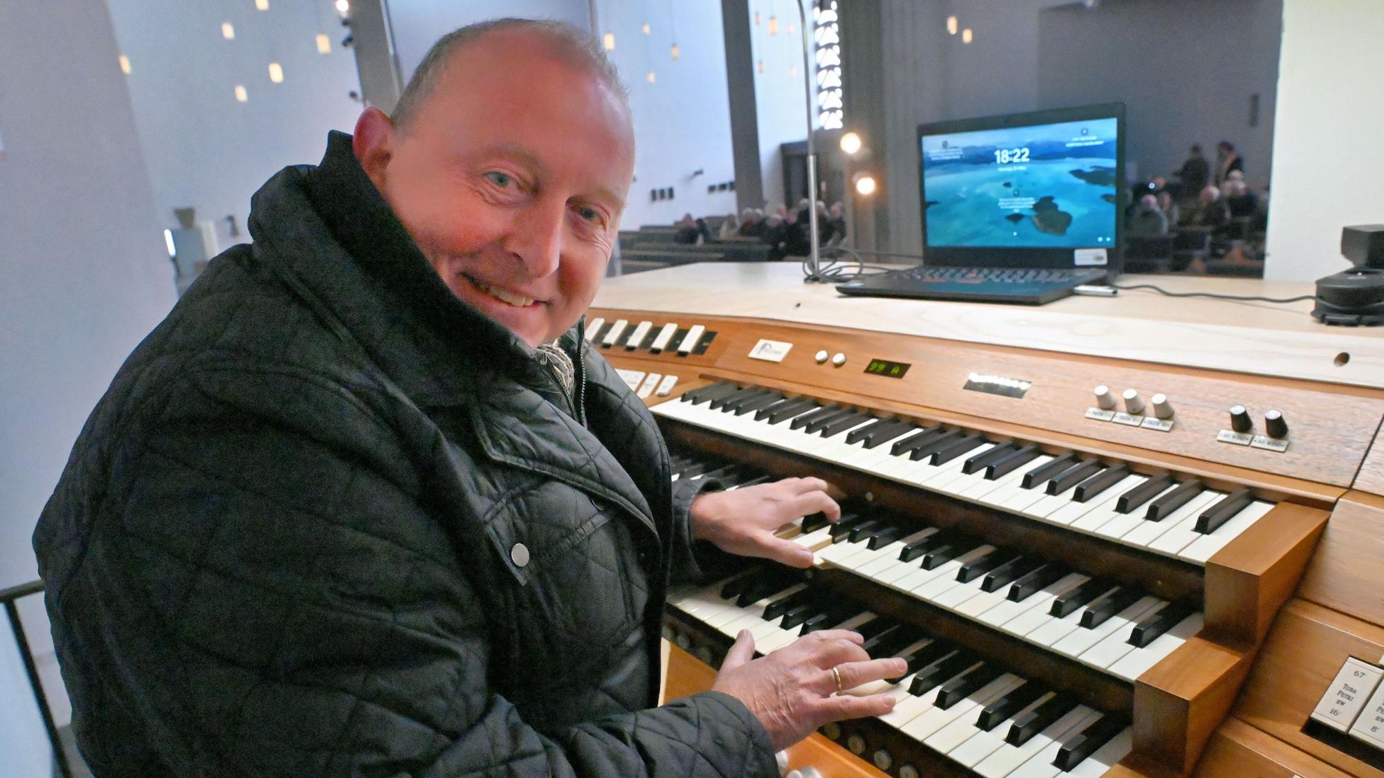 Otto Maria Krämer sitzt am Spieltisch der Orgel, auf dem ein Laptop steht. Der Organist hat eine dicke Jacke an.