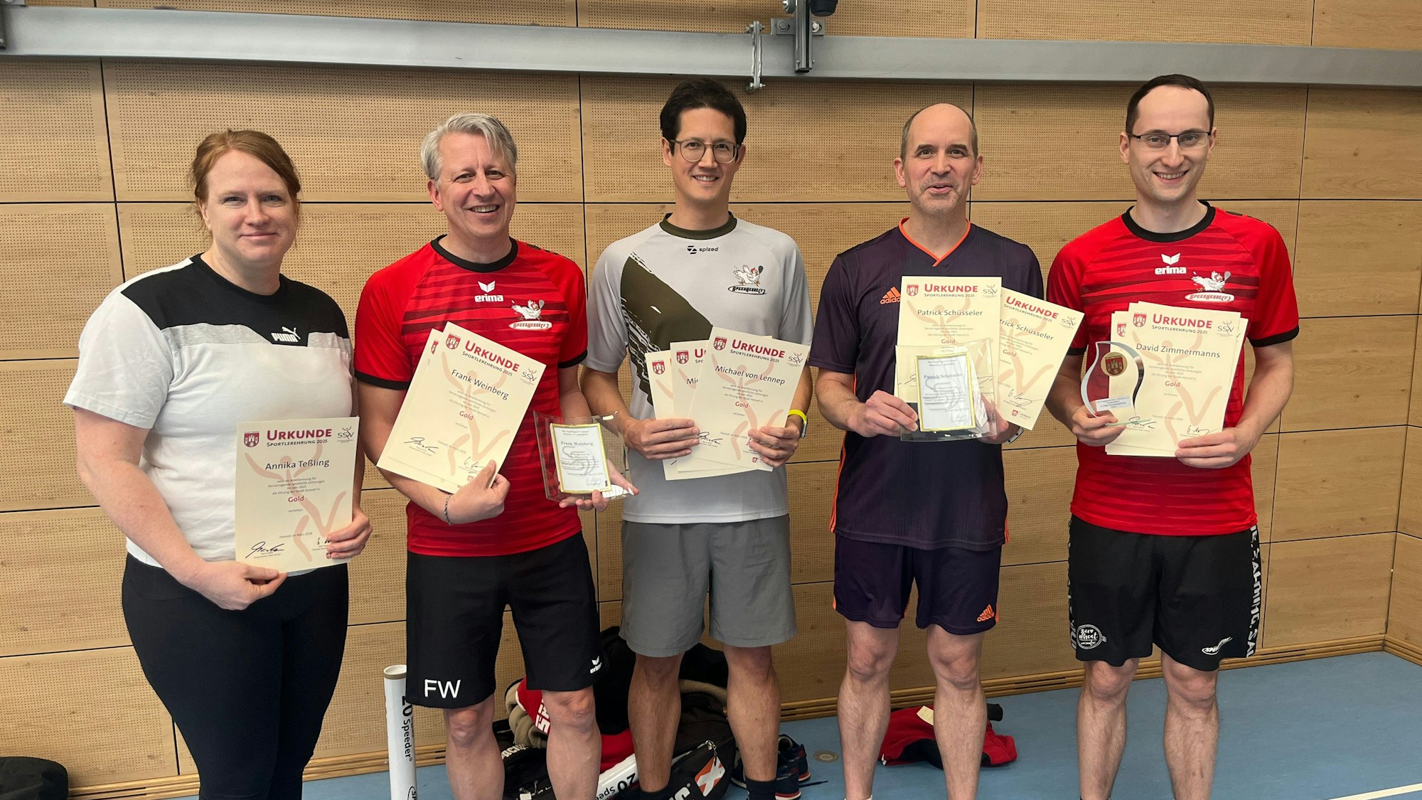 Die Sportler halten Auszeichnungen und Urkunden in der Hand und lächeln in die Kamera.