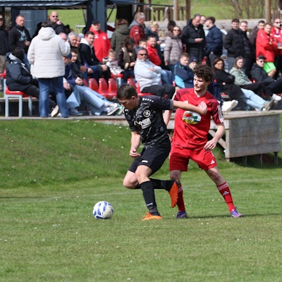 Simon Dürbaum (l.) wird von Mechernichs Marcel Zahn bedrängt. Im Hintergrund ist das Publikum zu sehen, das in der Sonne sitzt.
