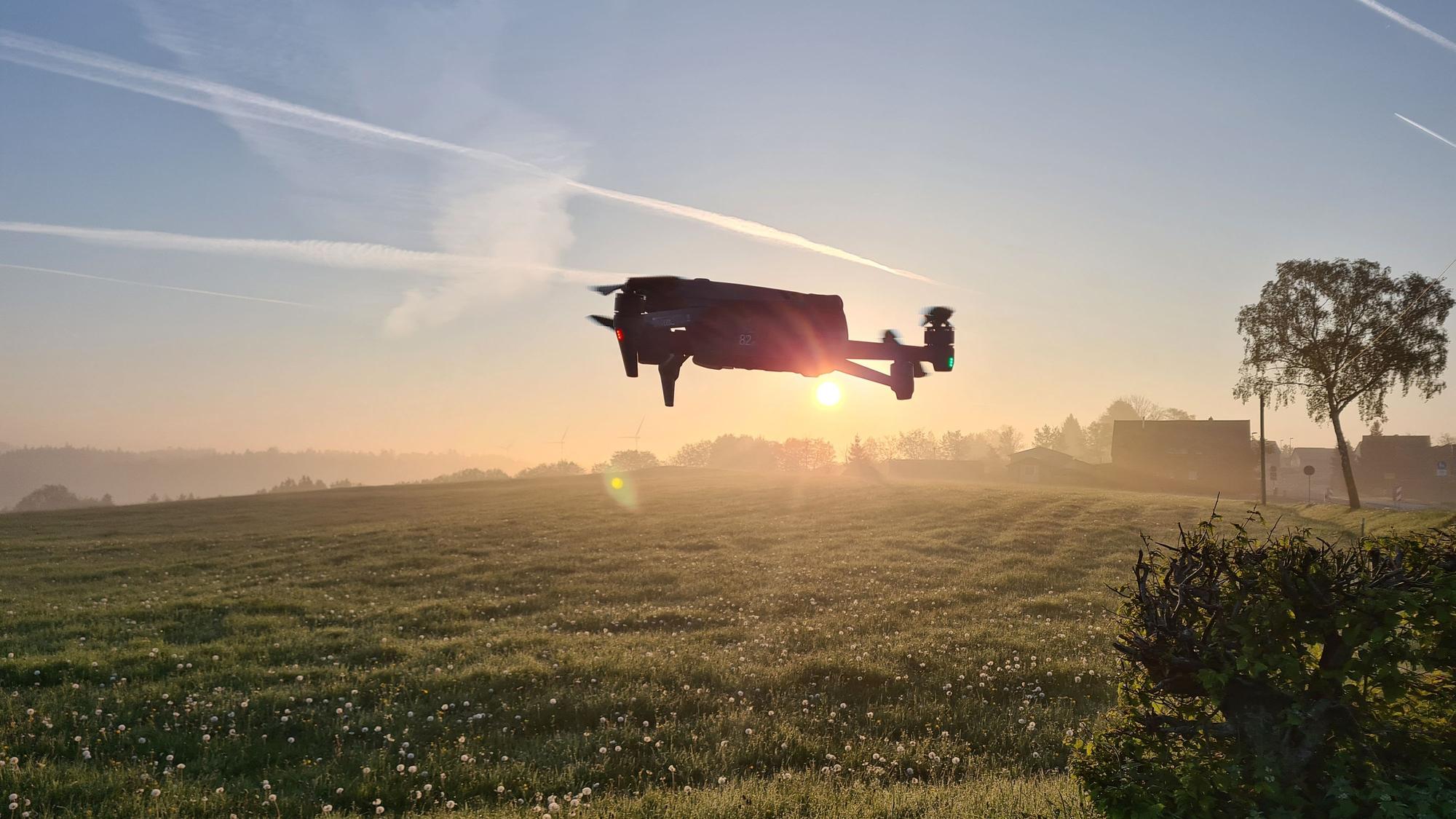 Eine Drohne steigt bei Sonnenaufgang über einer Wiese auf.