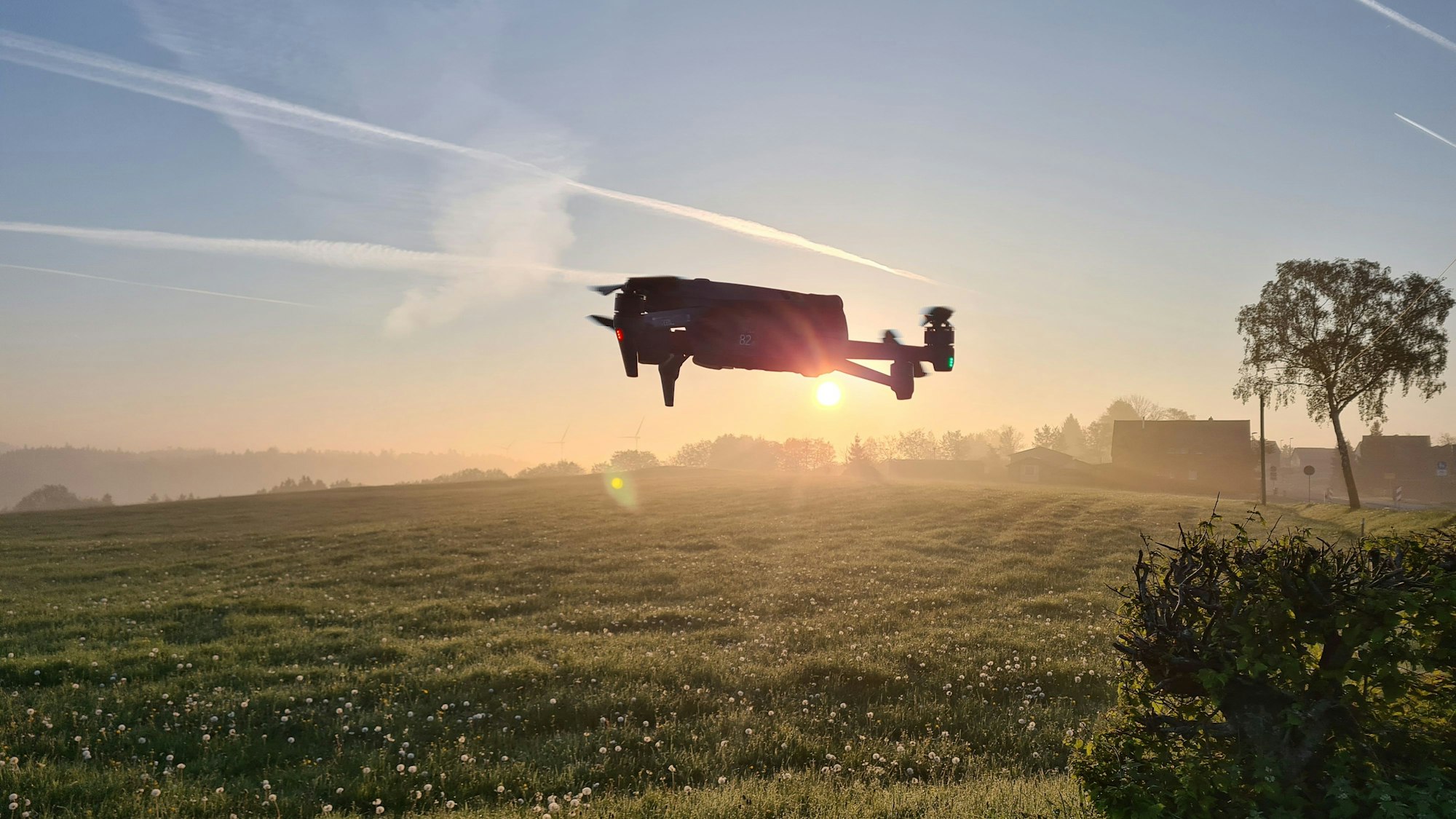Eine Drohne steigt bei Sonnenaufgang über einer Wiese auf.