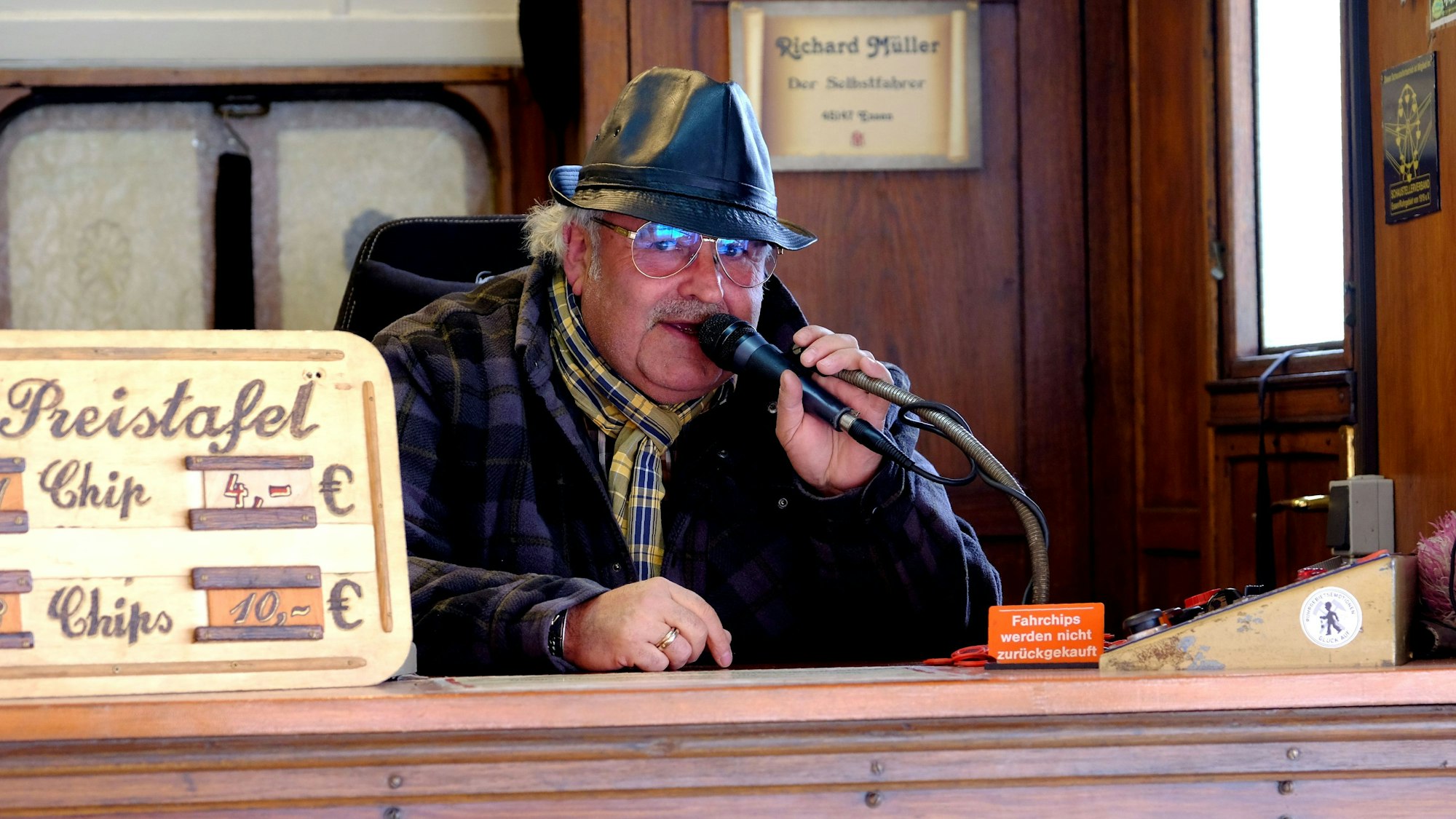 Ein Mann mit schwarzem Lederhut sitzt im Kassenhäuschen und spricht in ein Mikrofon.