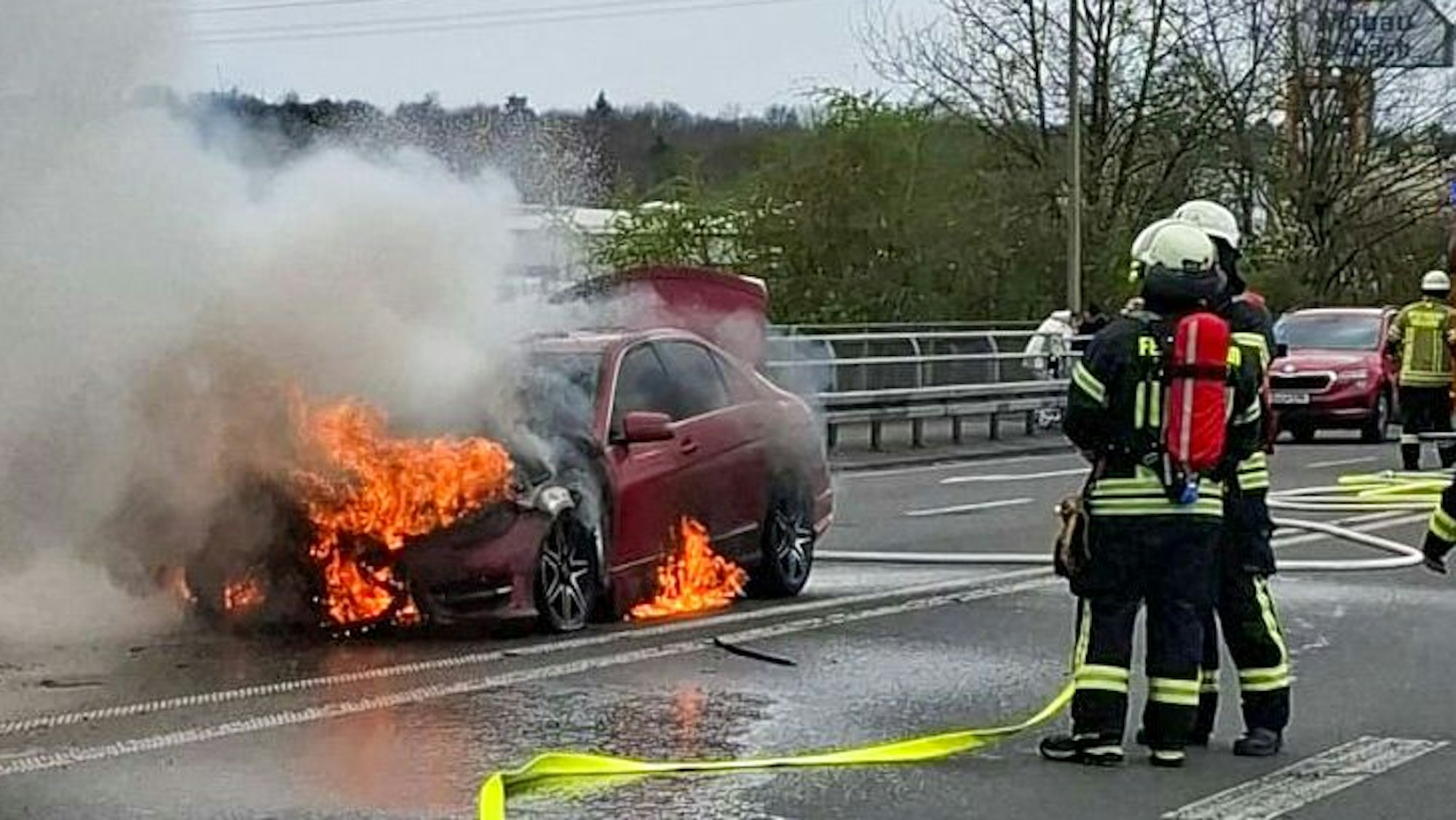 Feuerwehrleute stehen neben einem brennenden Auto.