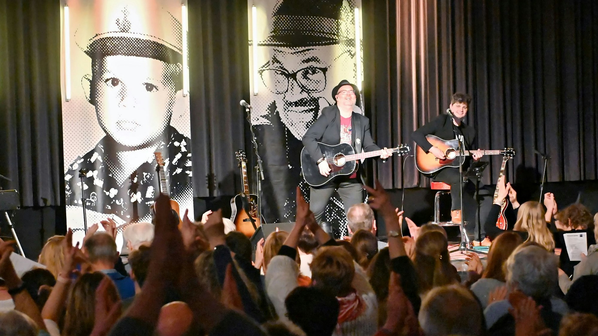 Auf der Bühne im Casino steht Björn Heuser mit seiner Band. An der Wand dahinter hängen große Banner mit Porträtfotos des Künstlers.