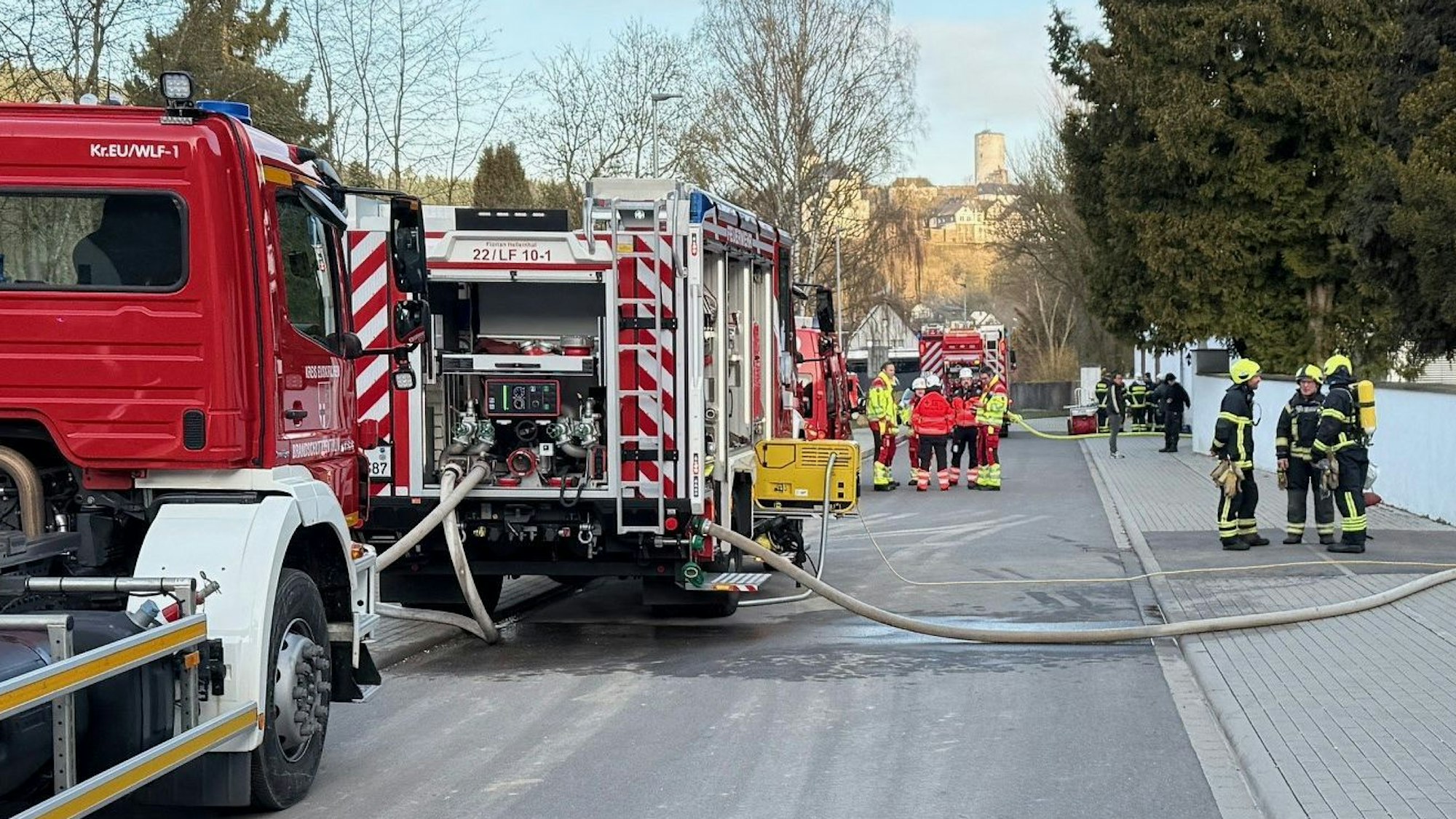 Einige Feuerwehrleute und ihre Einsatzfahrzeuge stehen auf einer Straße in Reifferscheid.