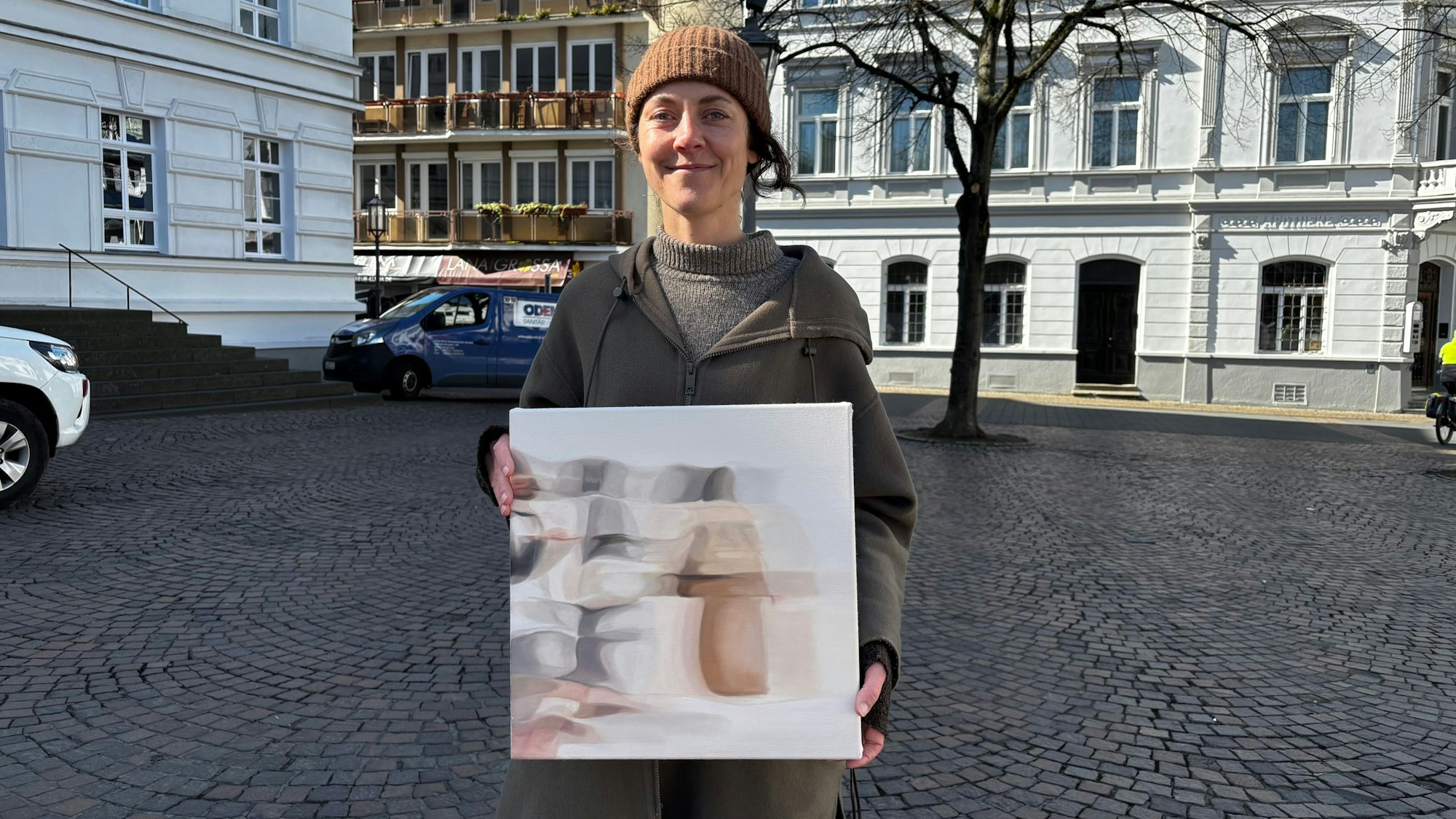Eine Frau hält ein kleineres Gemälde in der Hand.