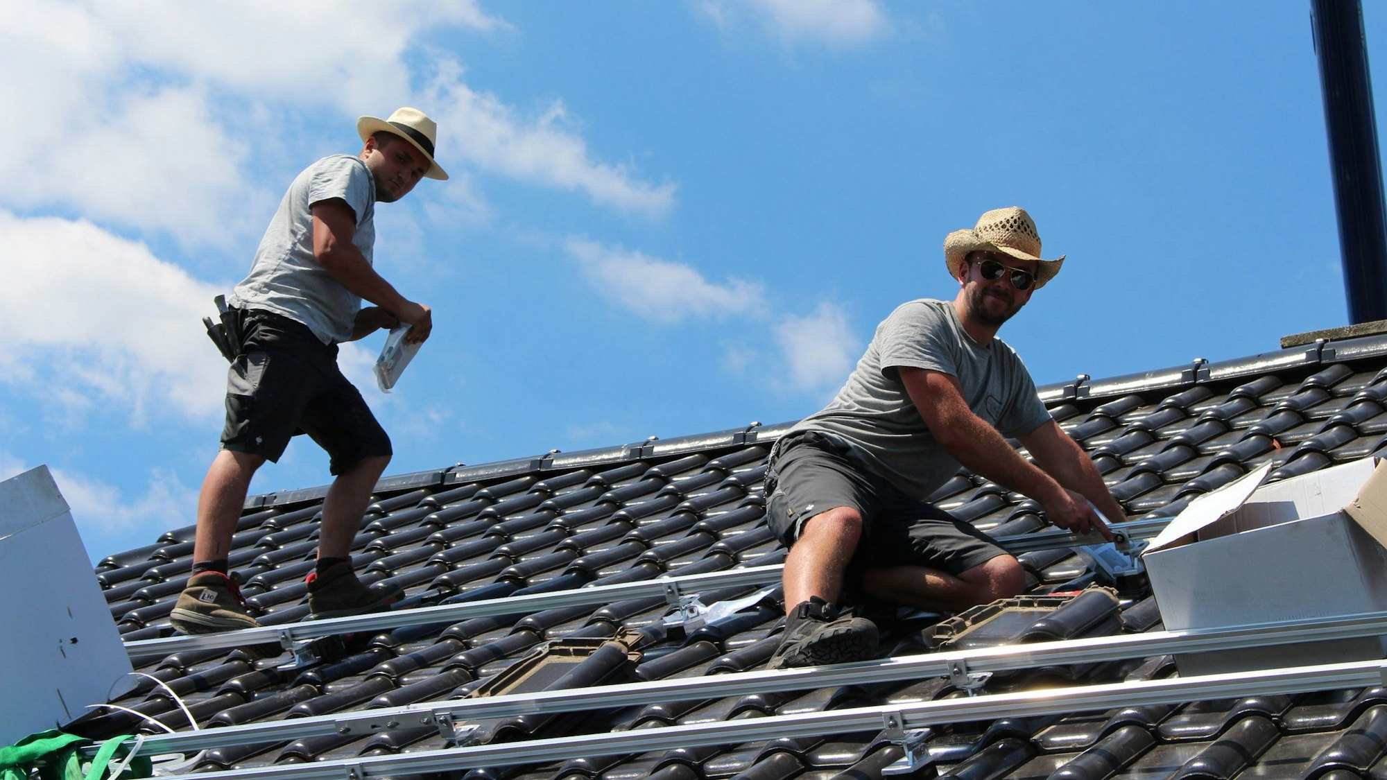 Zwei Männer arbeiten auf einem Dach. Sie montieren Halterungen für Solarpaneele.
