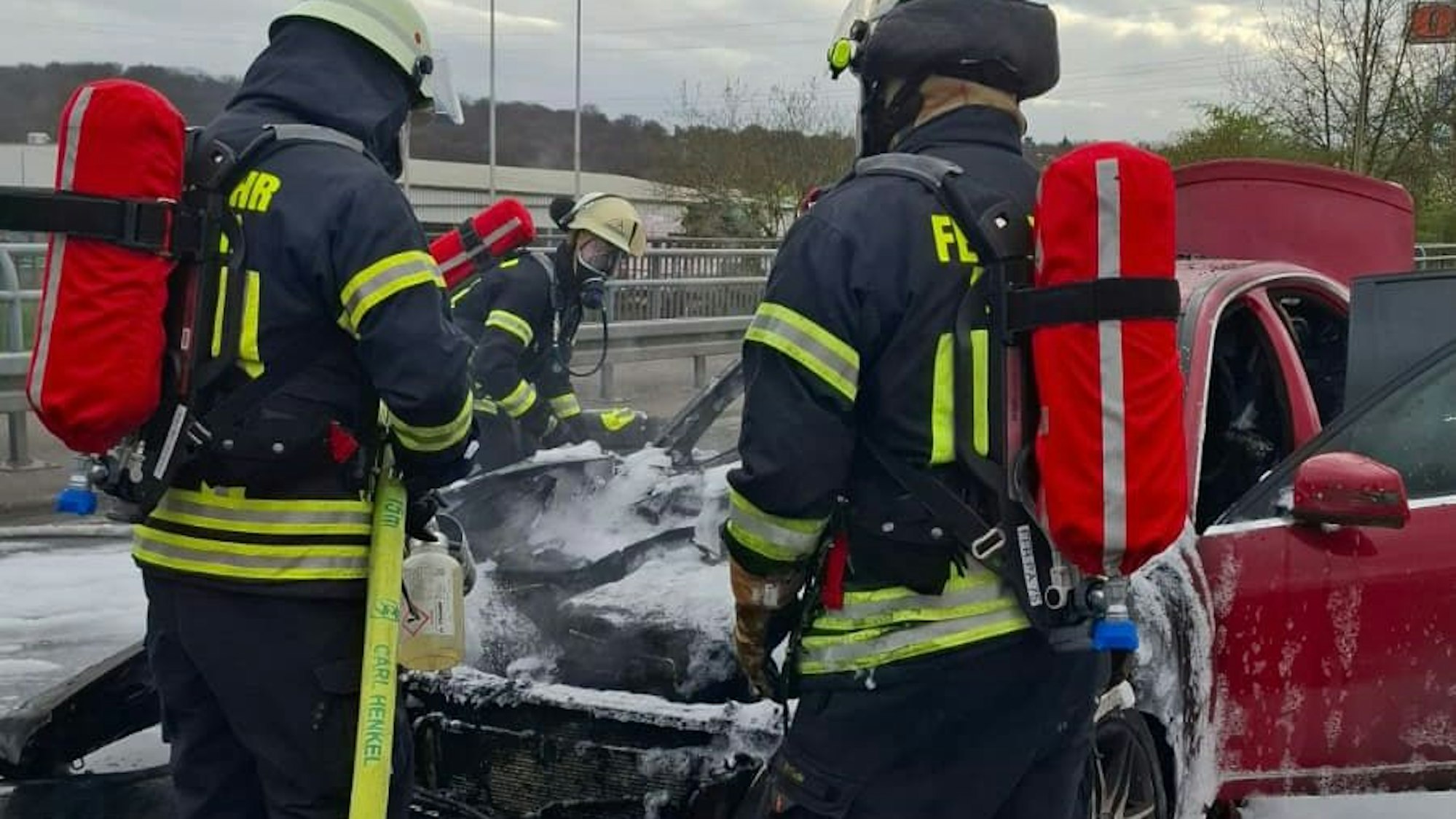 Drei Feuerwehrleute löschen ein Auto.