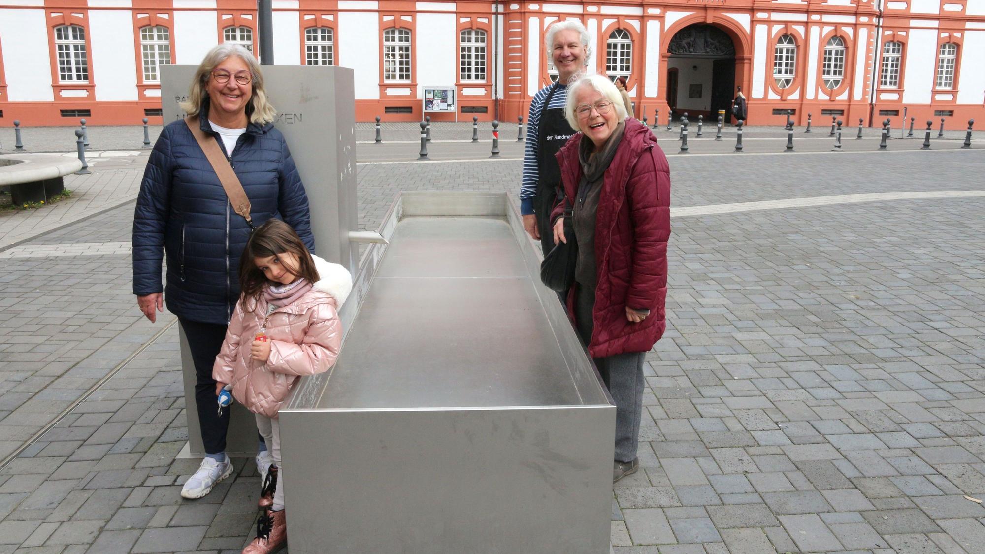 Drei Erwachsene und ein Kind stehen an einem Brunnen, Wasser sprudelt nicht.