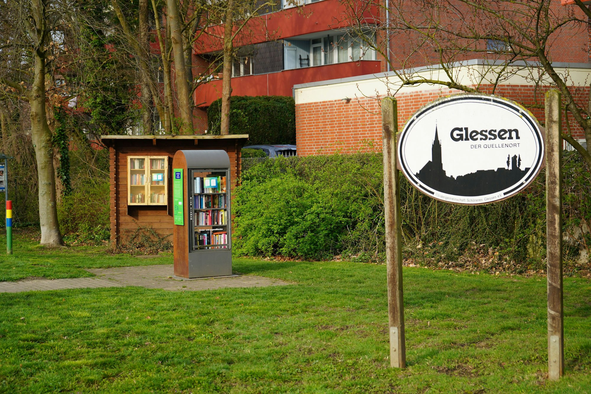 Das Bild zeigt ein Ortschild von Glessen und einen Bücherschrank.