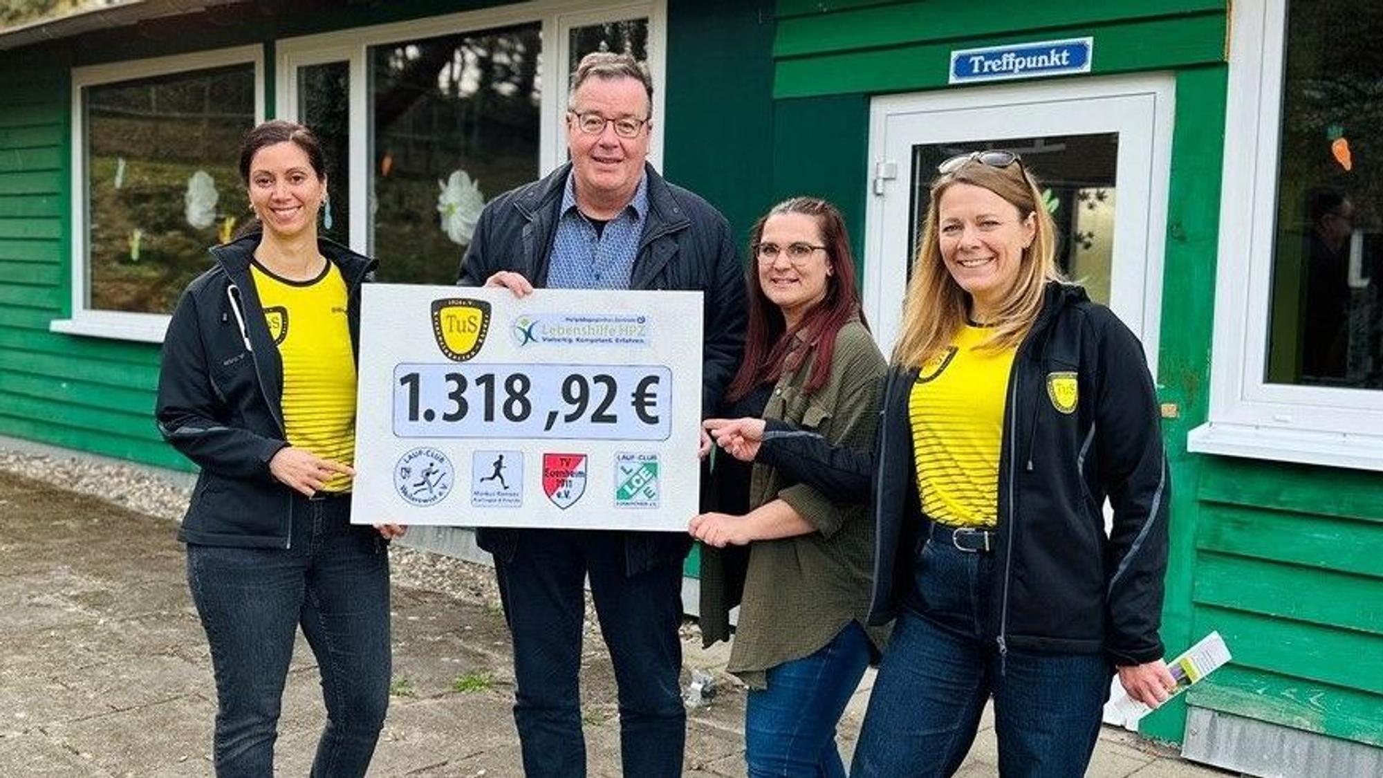 Zwei Vertreterinnen des TuS Kreuzweingarten-Rheder in gelben Trikots stehen mit einem Mann und einer Frau vor einer grünen Blockhütte.