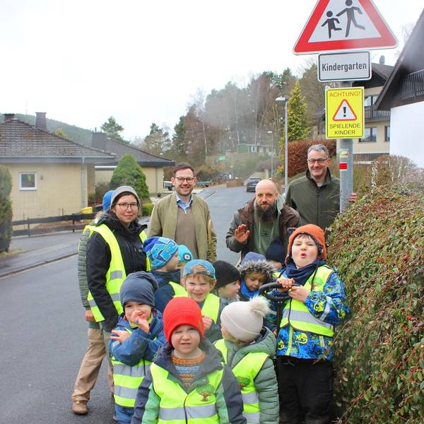 Das Bild zeigt drei Männer und eine Erzieherin mit den Kindern, die Warnwesten tragen.