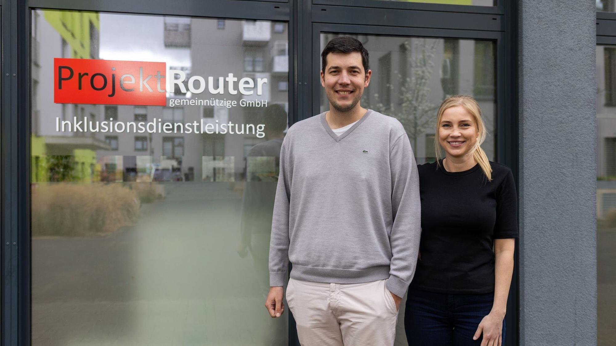 Ein Mann und eine Frau stehen vor einem Fenster mit der Aufschrift „Projekt Router“.