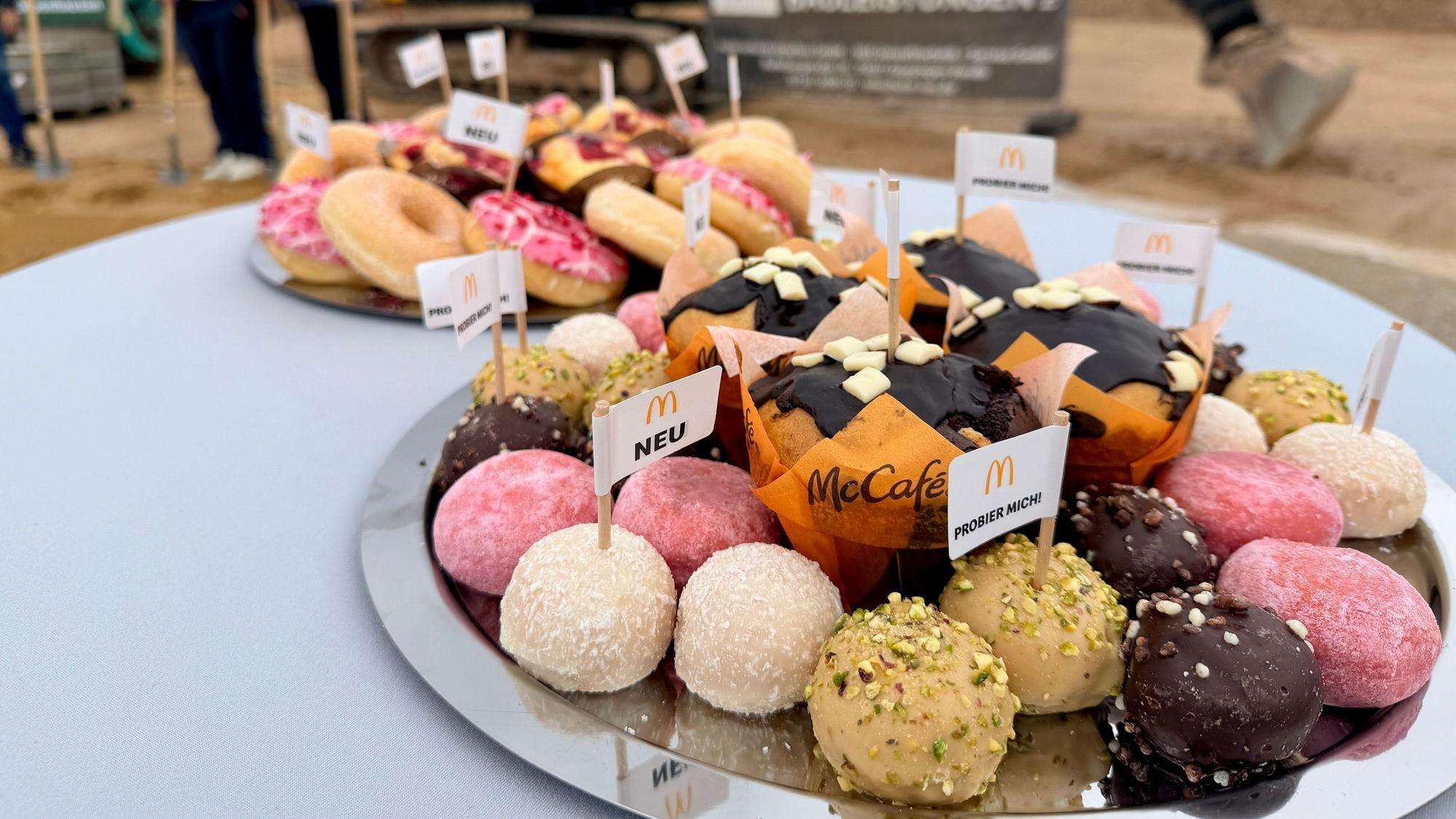 Muffins, Donuts und andere Leckereien von McDonald's, in denen kleine Fähnchen stecken, liegen auf einem Teller.