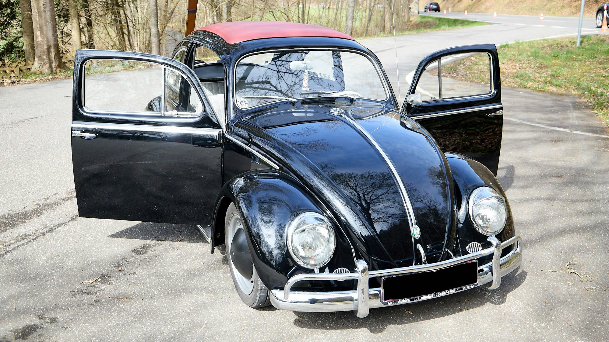 Der schwarze Käfer mit rotem Stoffdachz steht mit geöffneten Türen auf dem Parkplatz.