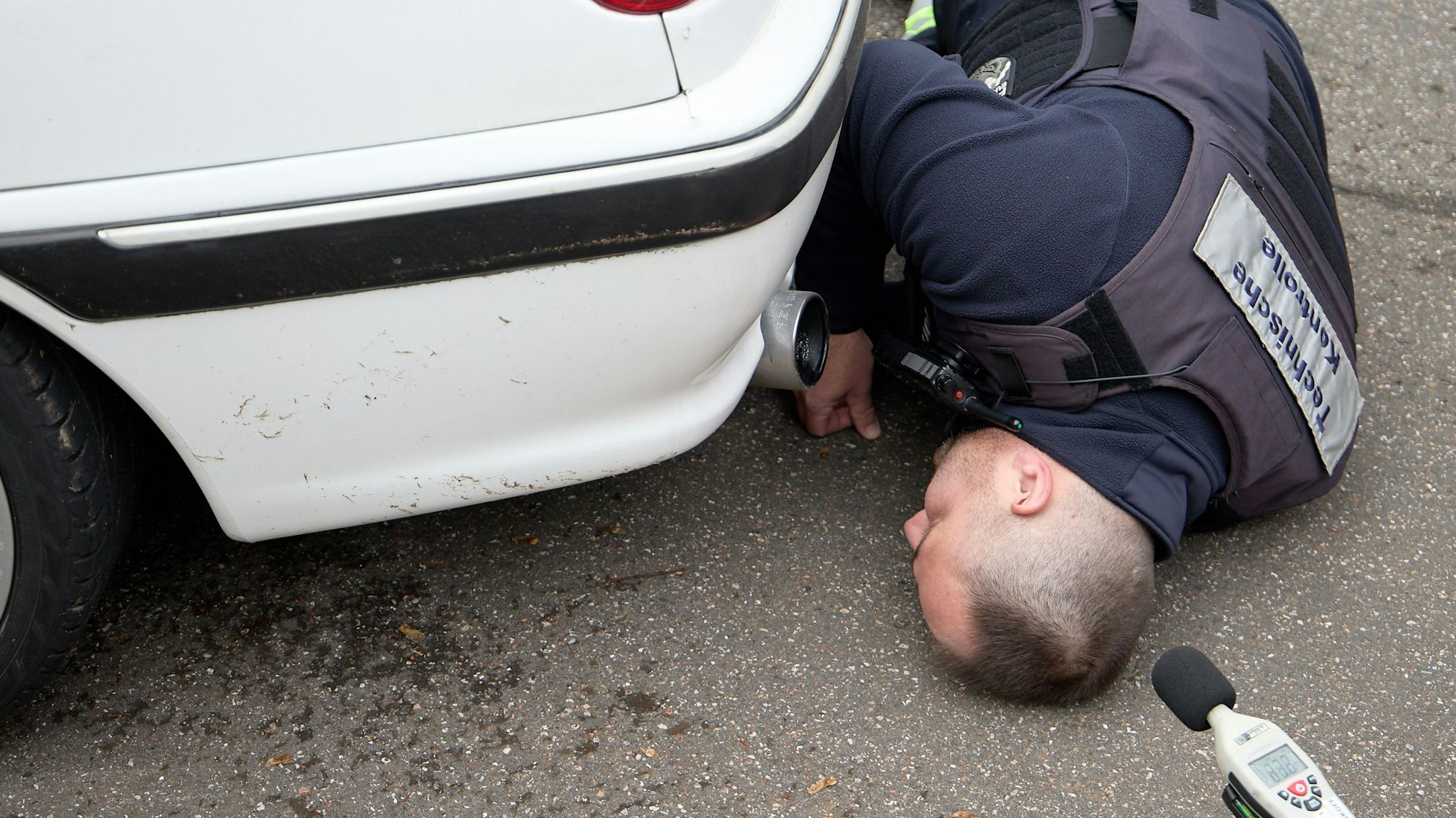 Weber schaut unter eine Auto. Im Vordergrund ein Lärmmessgerät.