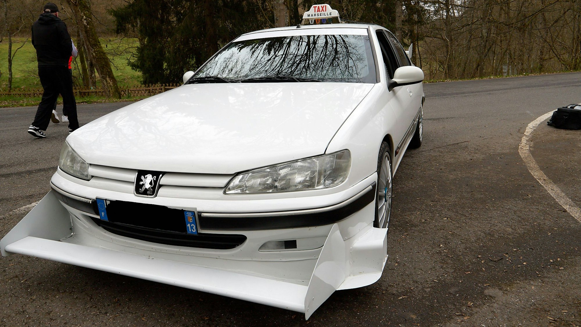 Ein weißer Peugeot 406 mit Taxi-Schild und einem großen, scharfkantigem Frontspoiler.