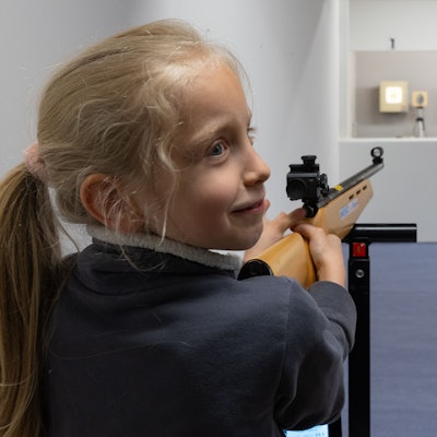 Ein Mädchen zielt mit einem Laser-Lichtpunkt-Gewehr auf eine Zielschiebe mit einem Osterei.