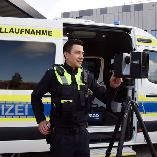 Zu sehen ist ein Polizist vor einem Polizeiwagen, der einen Scanner bedient.