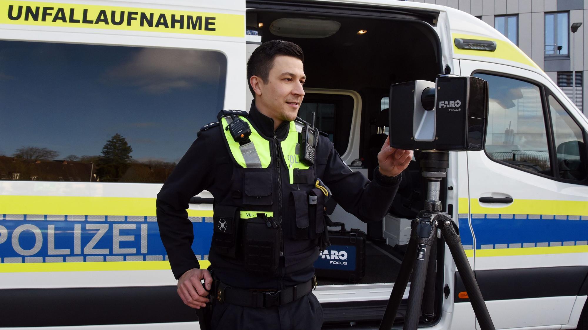 Zu sehen ist ein Polizist vor einem Polizeiwagen, der einen Scanner bedient.